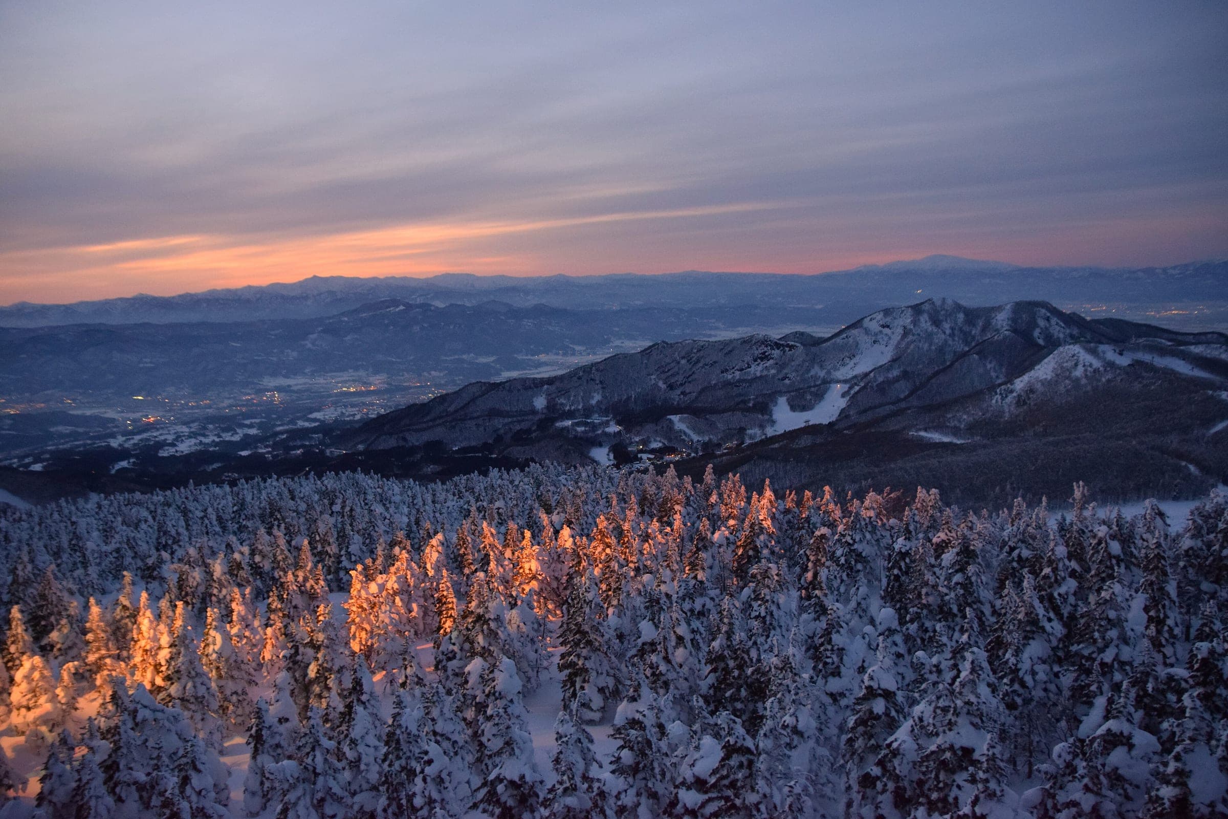 Last light turns the frosted trees orange above Zao Onsen with the Yamagata basin fading below.