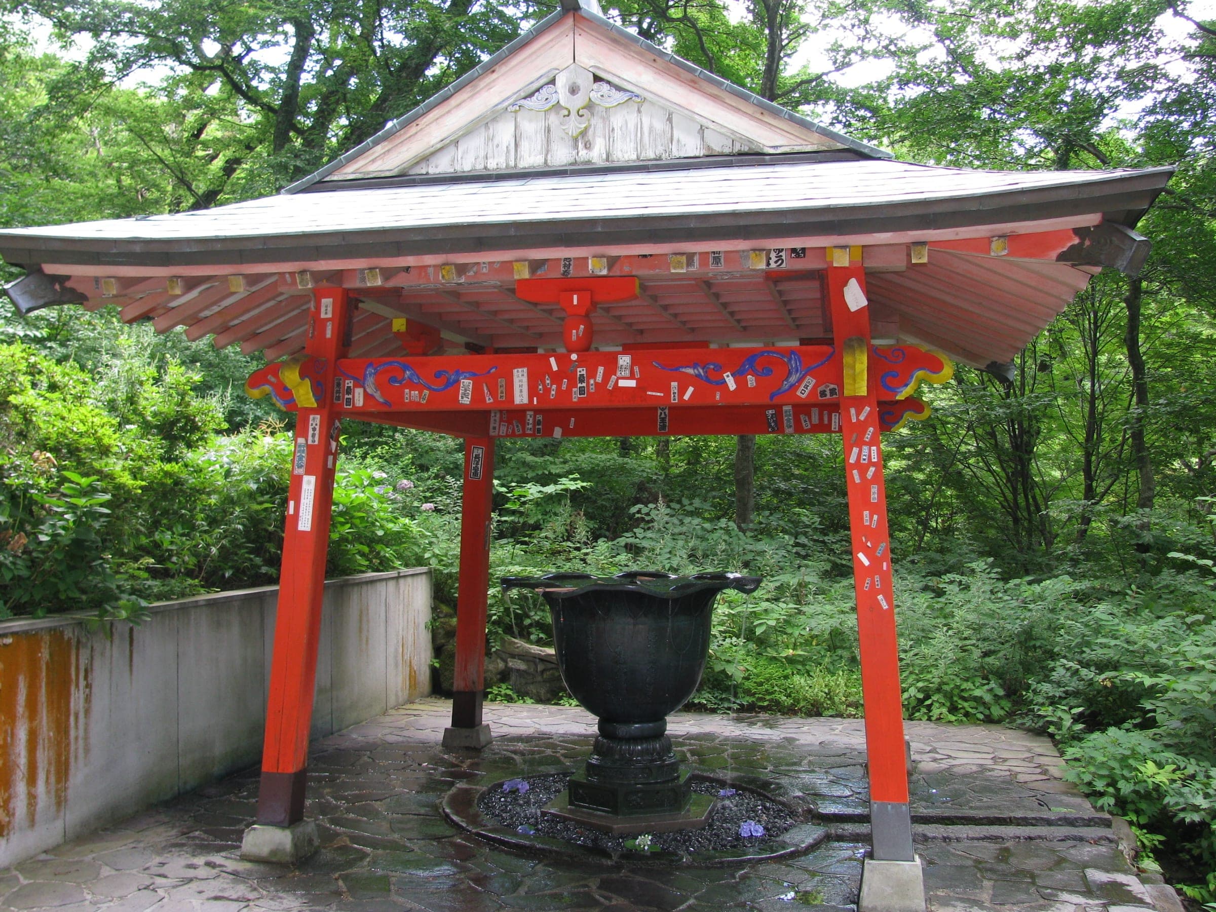 A red-painted pavilion with a bronze basin stands in the forest at Daisen-ji in August