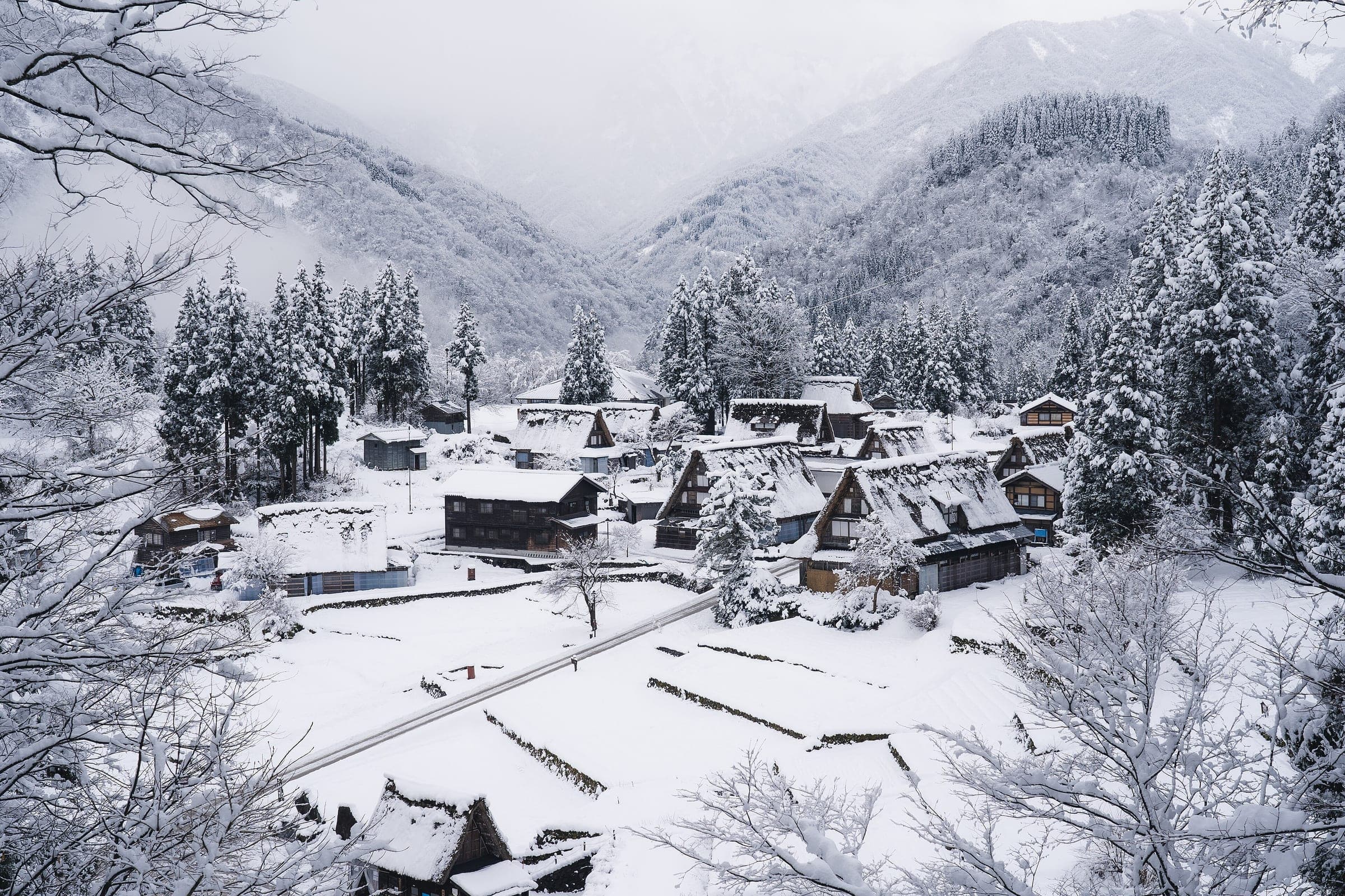 Snow buries the steep thatched roofs of Ainokura village in Gokayama below wooded mountains in February