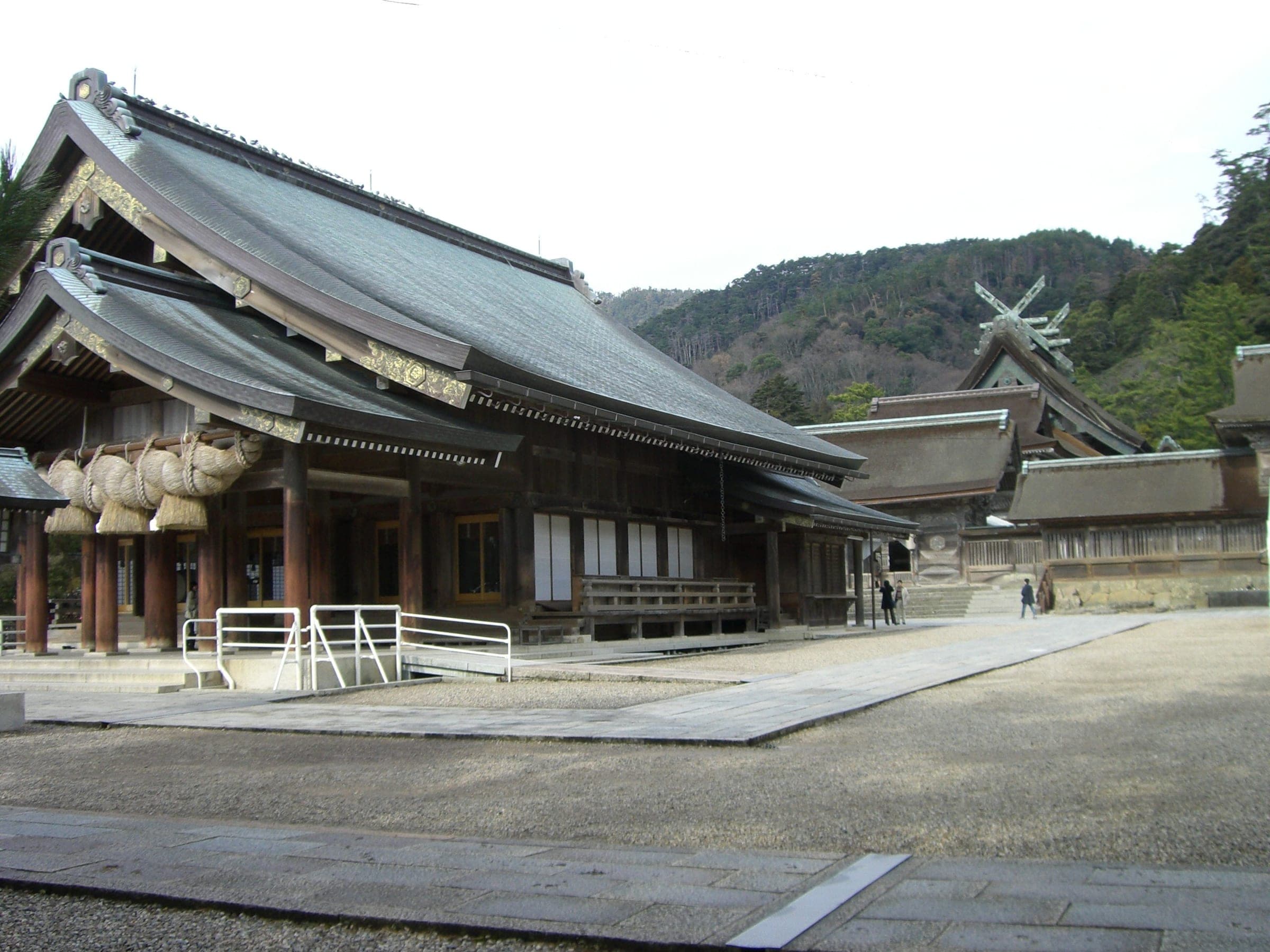 The Haiden roof and the crossed finials of the Honden rise behind it at Izumo Taisha in December