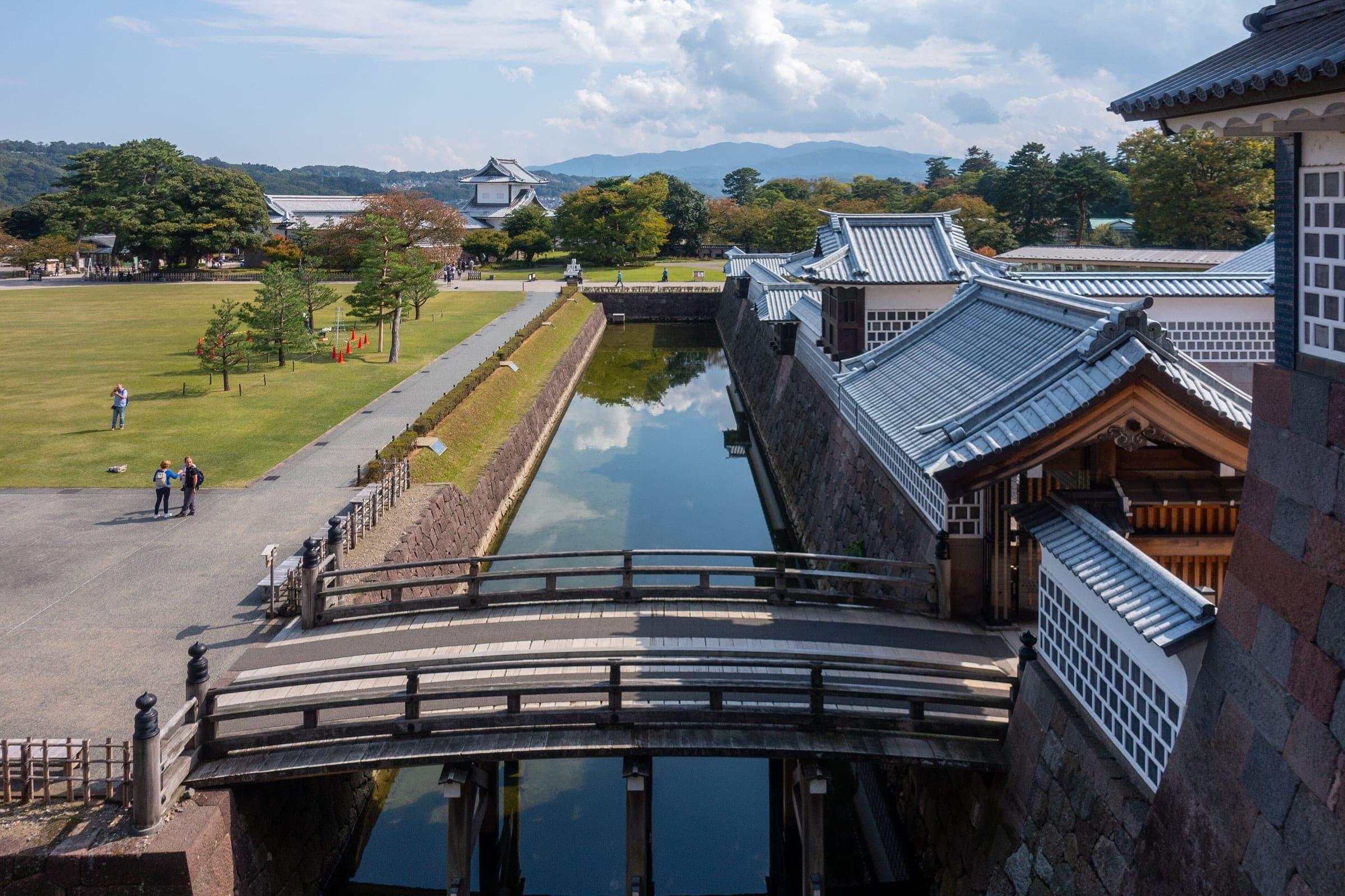 Hashizume bridge crosses the moat at Kanazawa Castle beside white-walled turrets and the castle lawns