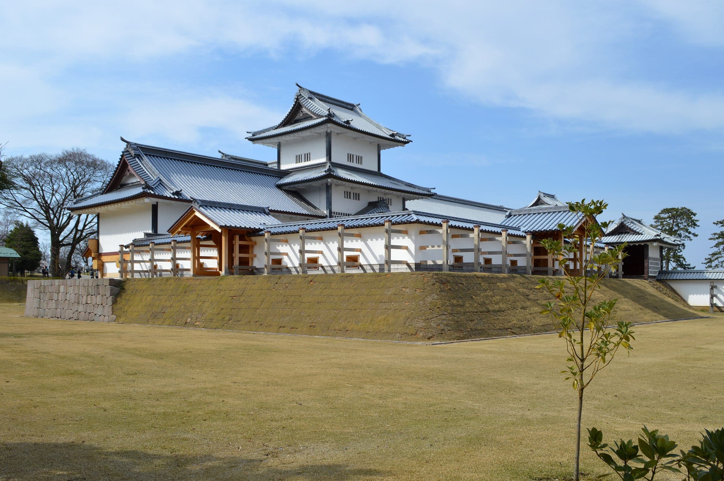 The white turret and long storehouse of Kanazawa Castle stand on a grassy stone base in spring