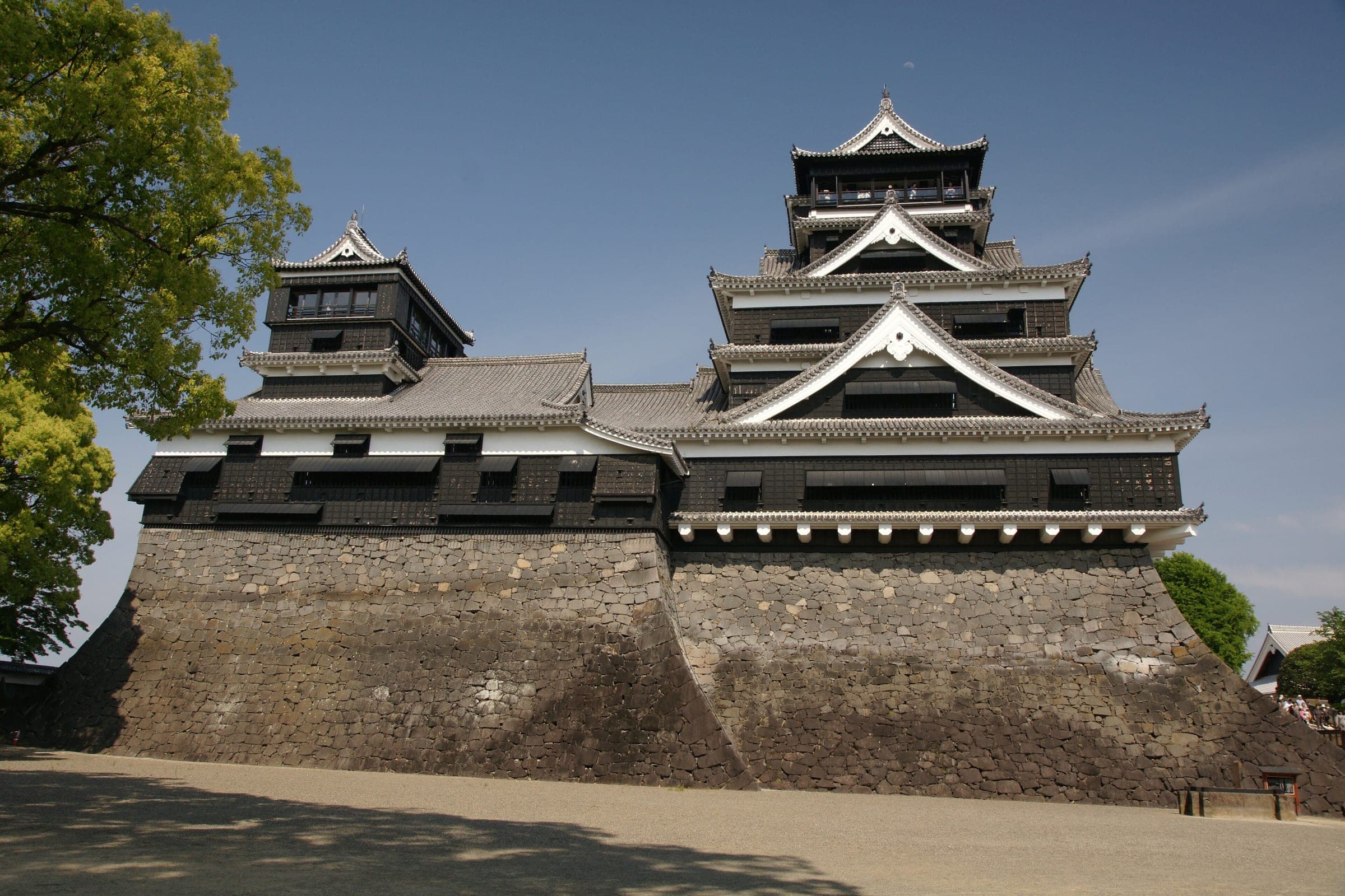 The large and small keeps of Kumamoto Castle rise over steep musha-gaeshi stone walls under a blue sky.