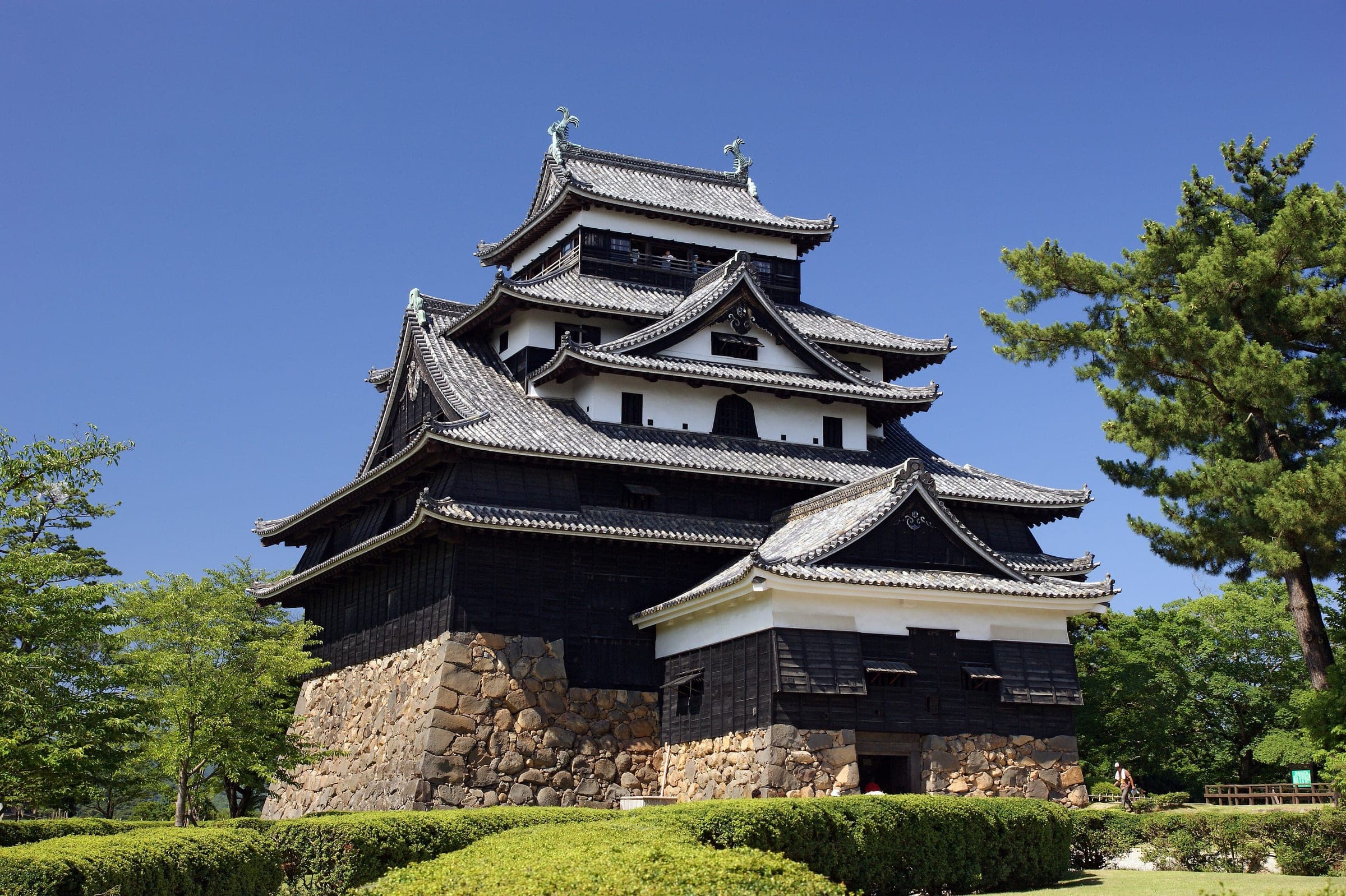 Matsue Castle's black-boarded keep stands on its stone base above clipped hedges in July