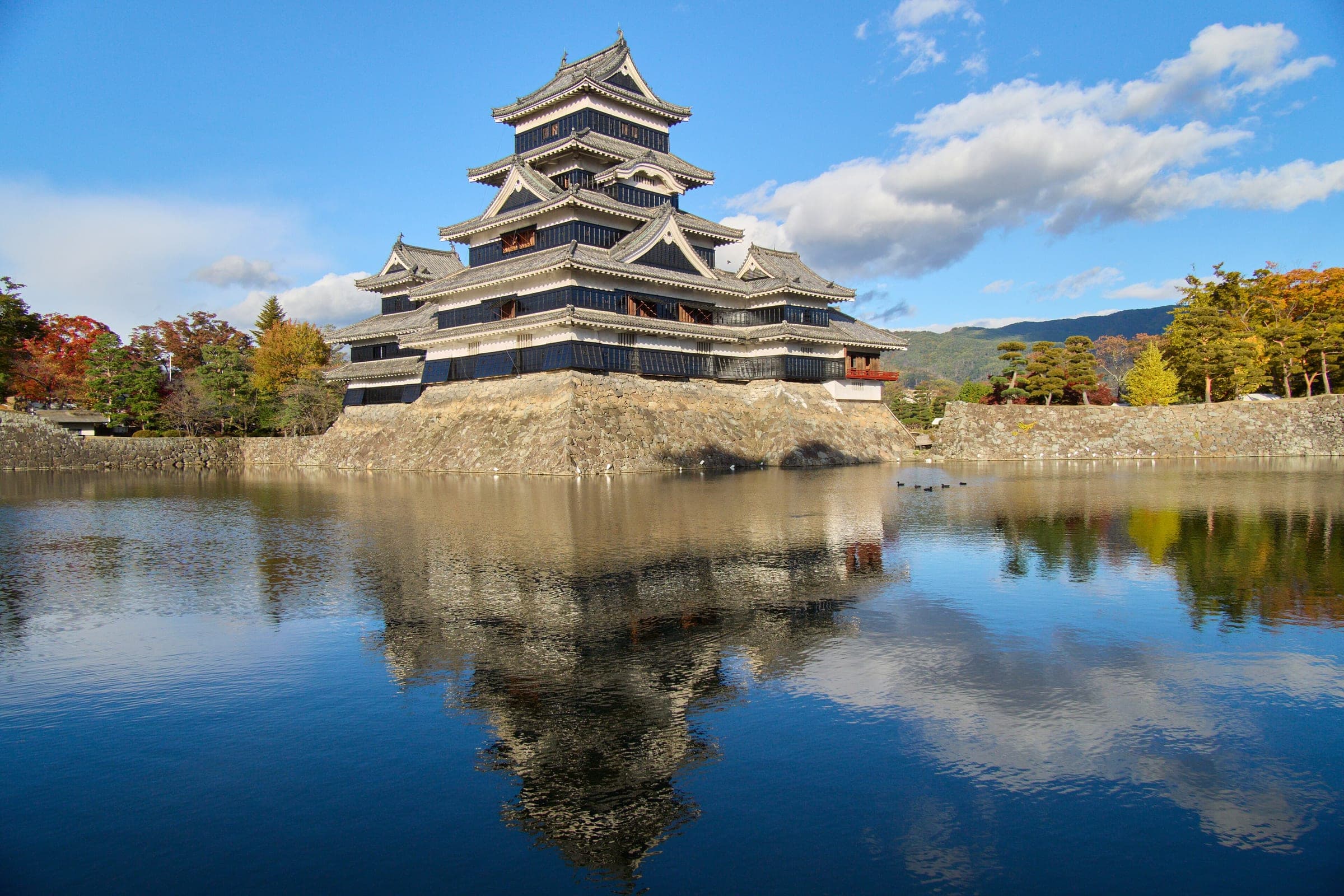 Matsumoto Castle's keep and turrets reflect in the still moat under a clear autumn sky.