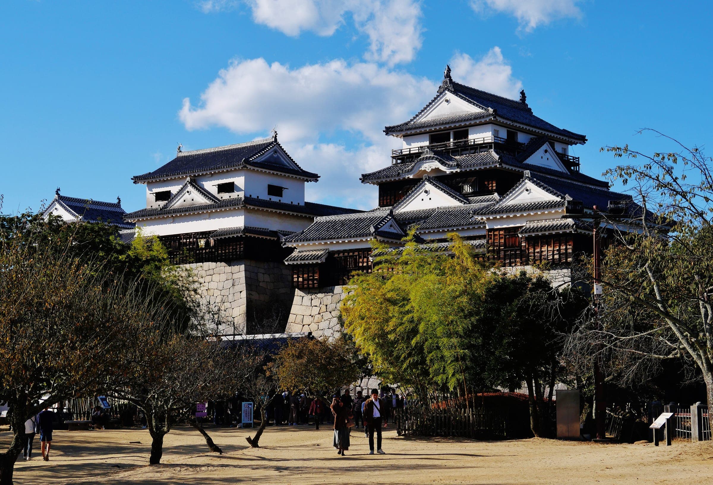 The white keep of Matsuyama Castle rises above its stone walls and the hilltop courtyard.