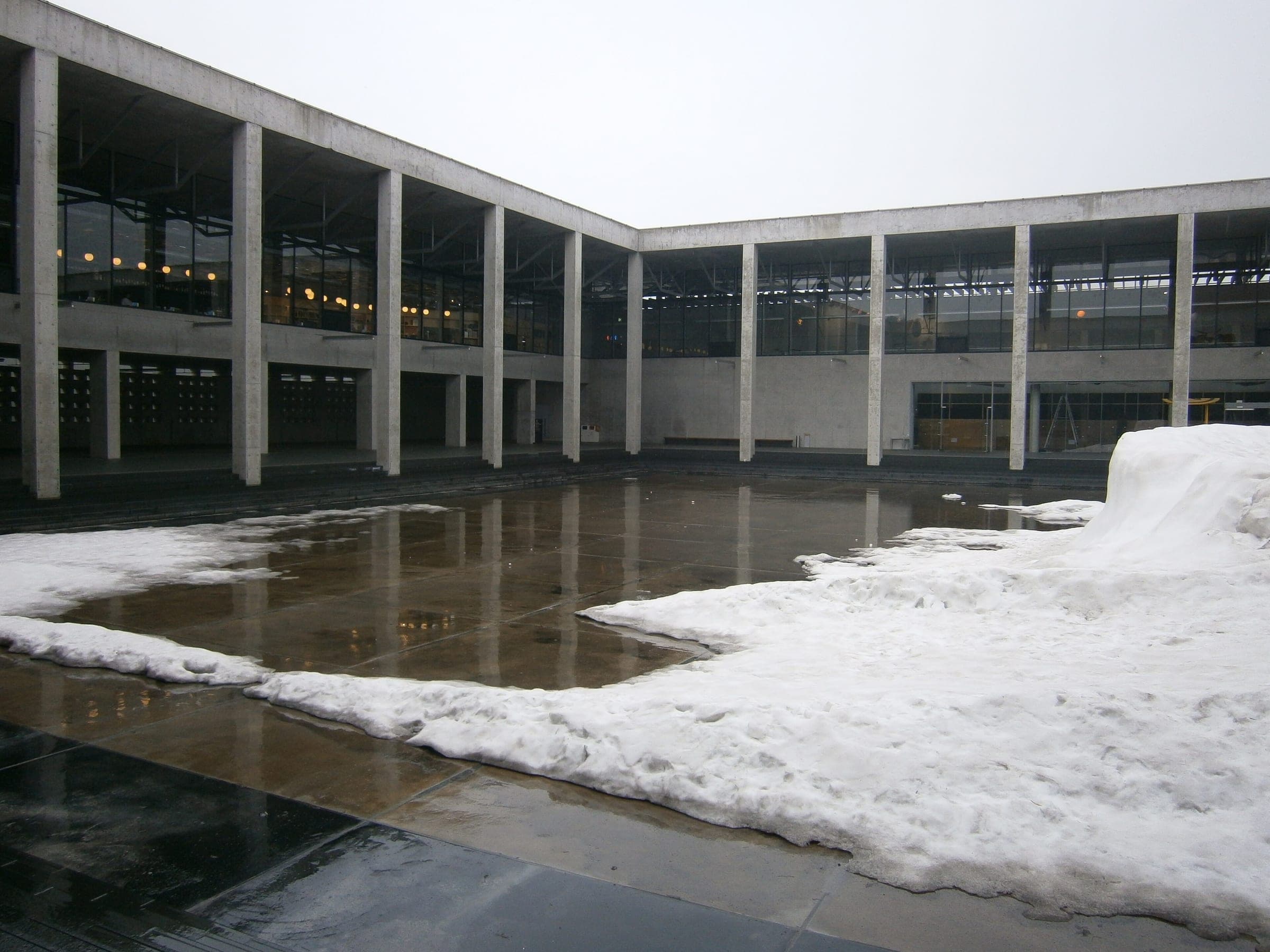 Late snow melts into the courtyard pool framed by the concrete colonnade of MonET in Tokamachi