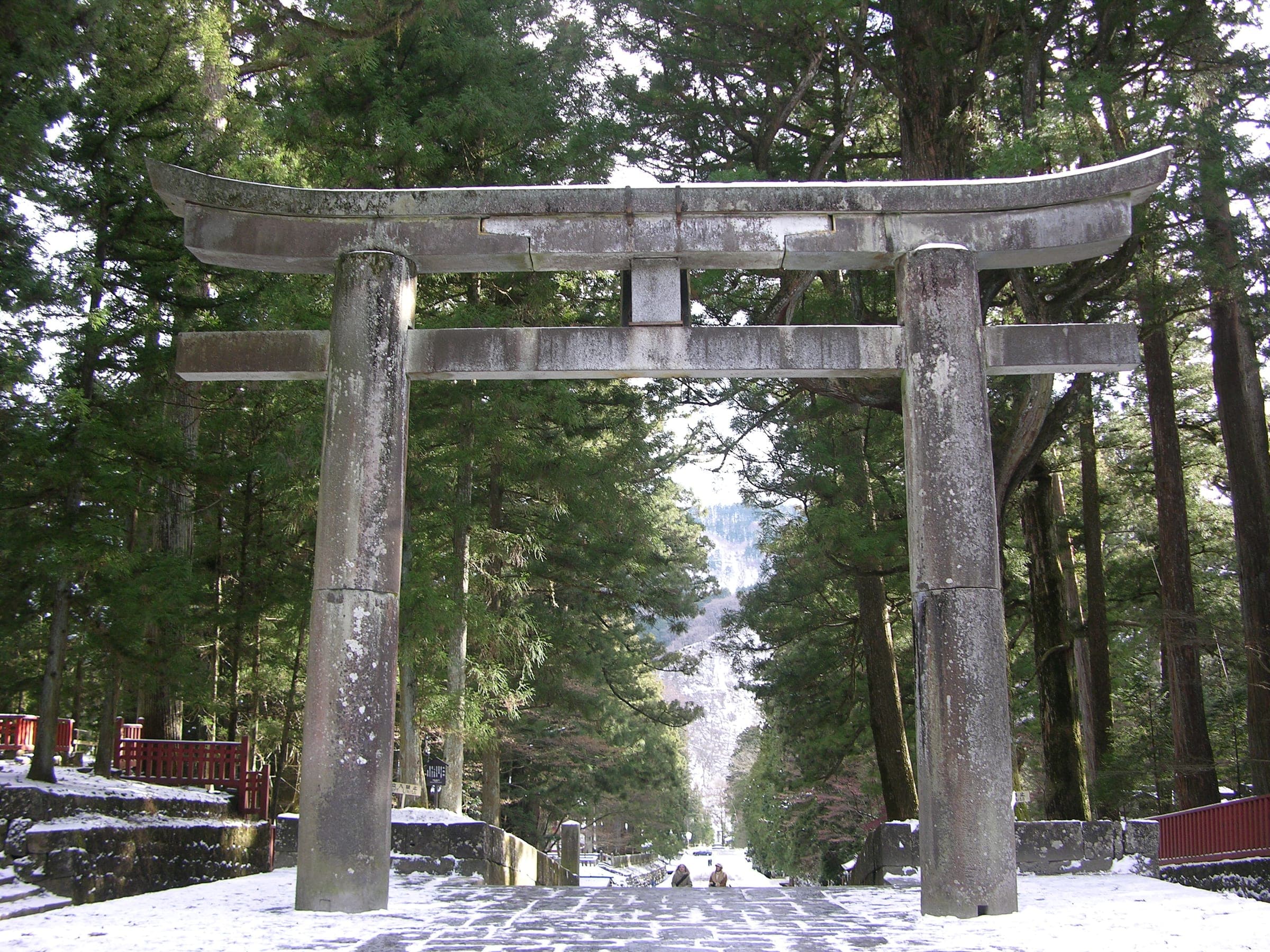 Snow lies on the approach under the stone torii at Nikko Toshogu among tall cedars