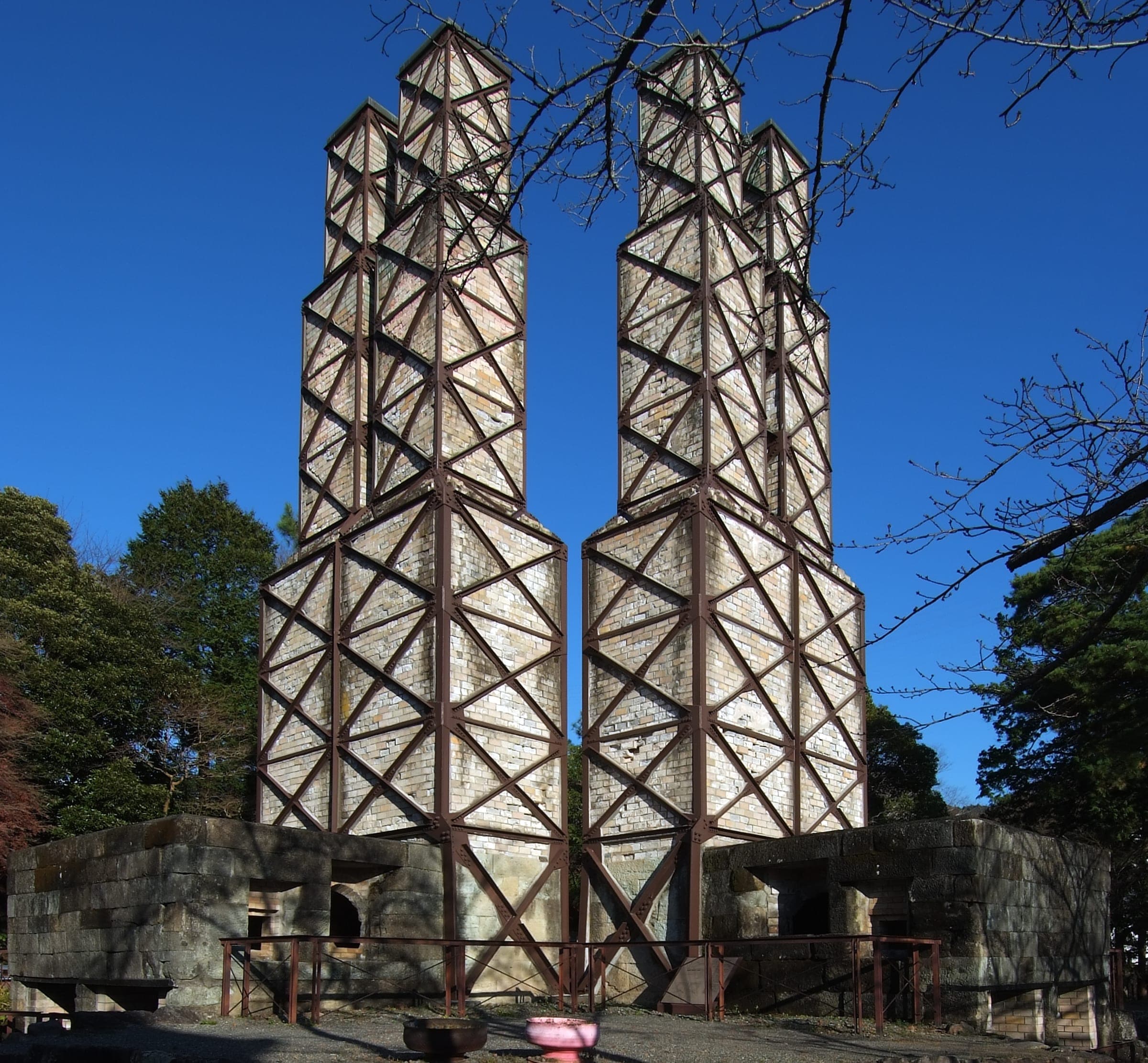 The twin brick chimneys of the Nirayama Reverberatory Furnace stand in steel bracing under a winter sky.