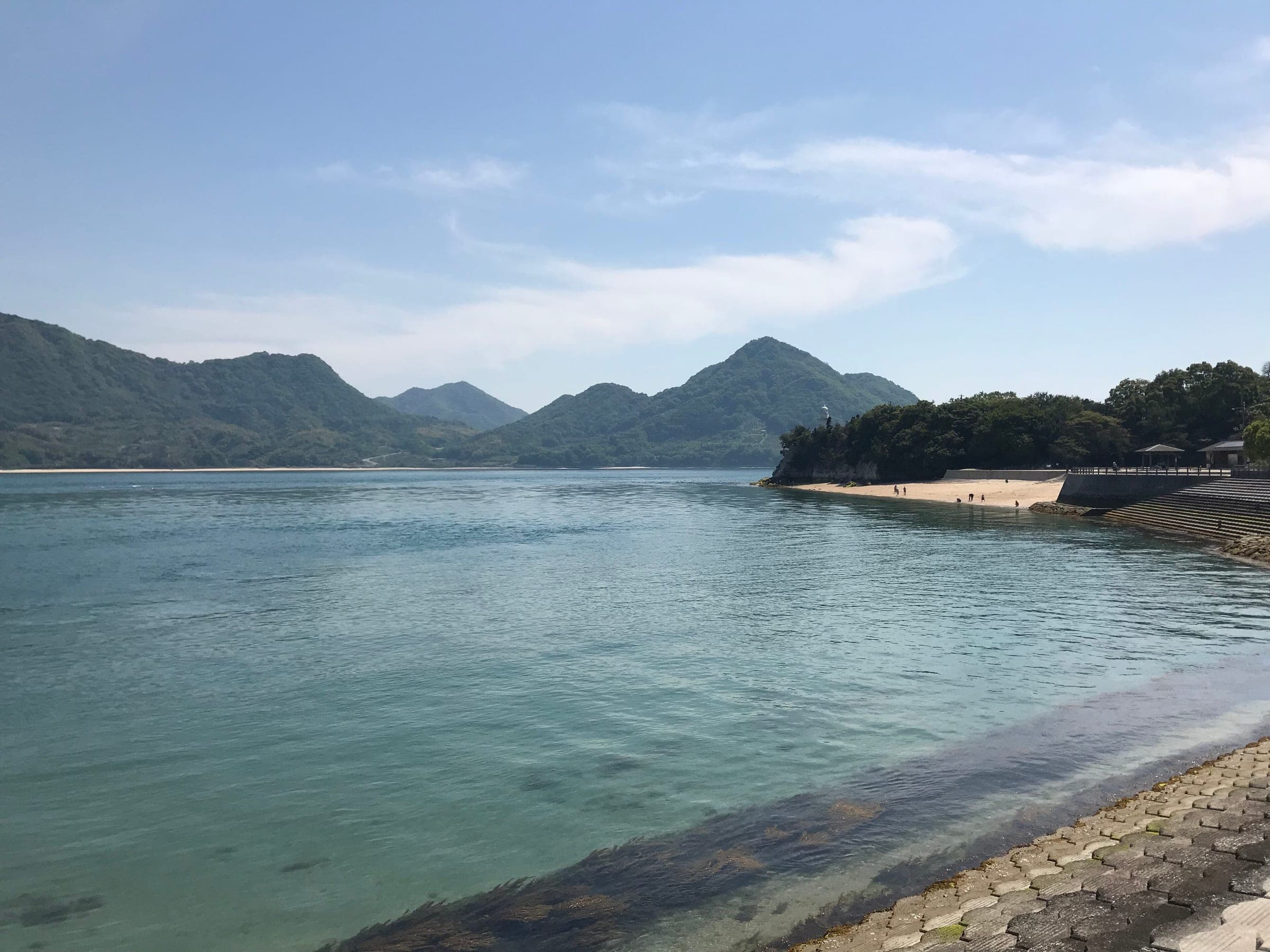 Clear water laps the beach on Okunoshima, with the hills of Omishima across the strait.