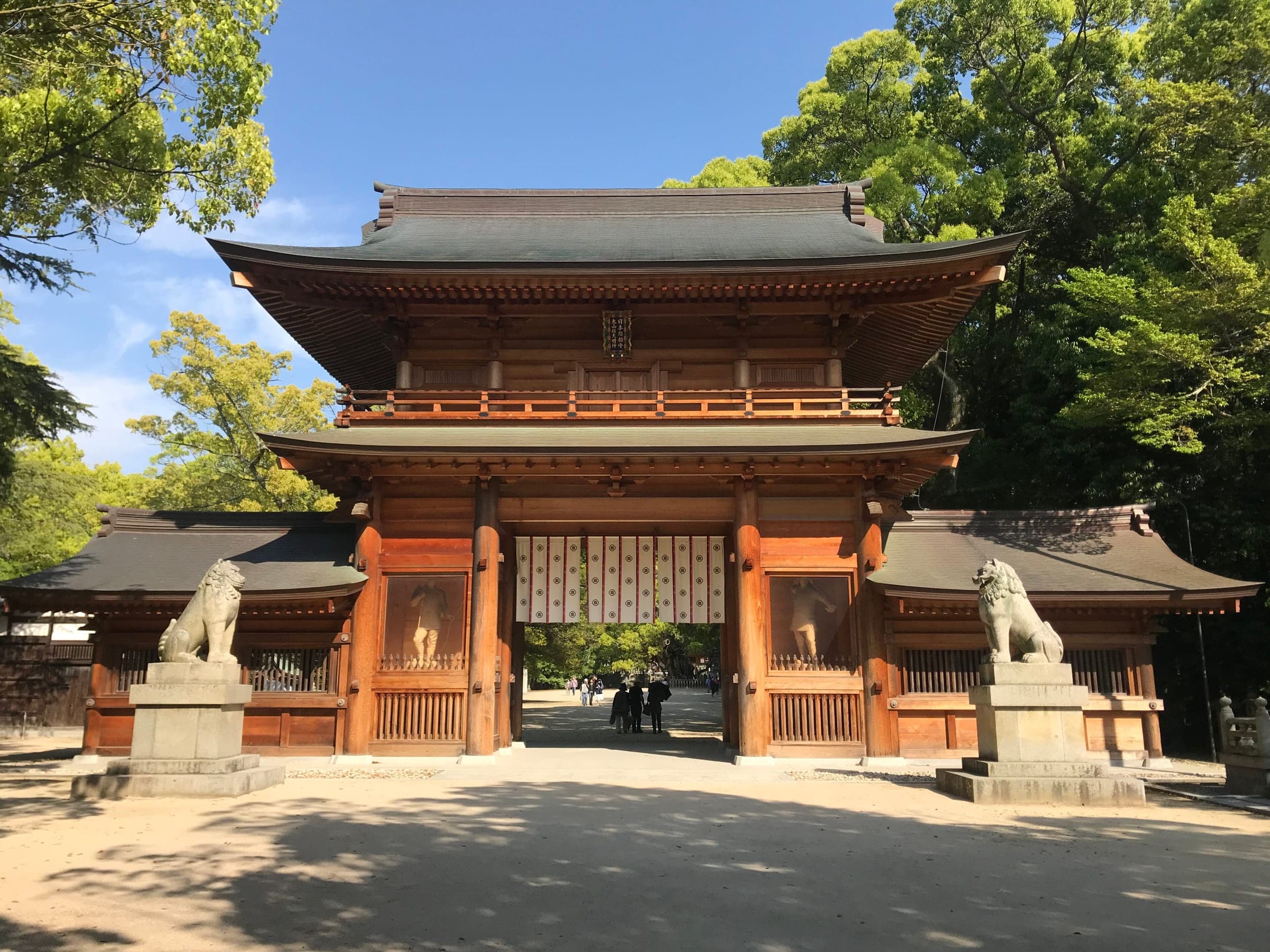 The vermilion two-storey Somon gate of Oyamazumi Shrine stands among camphor trees on Omishima.