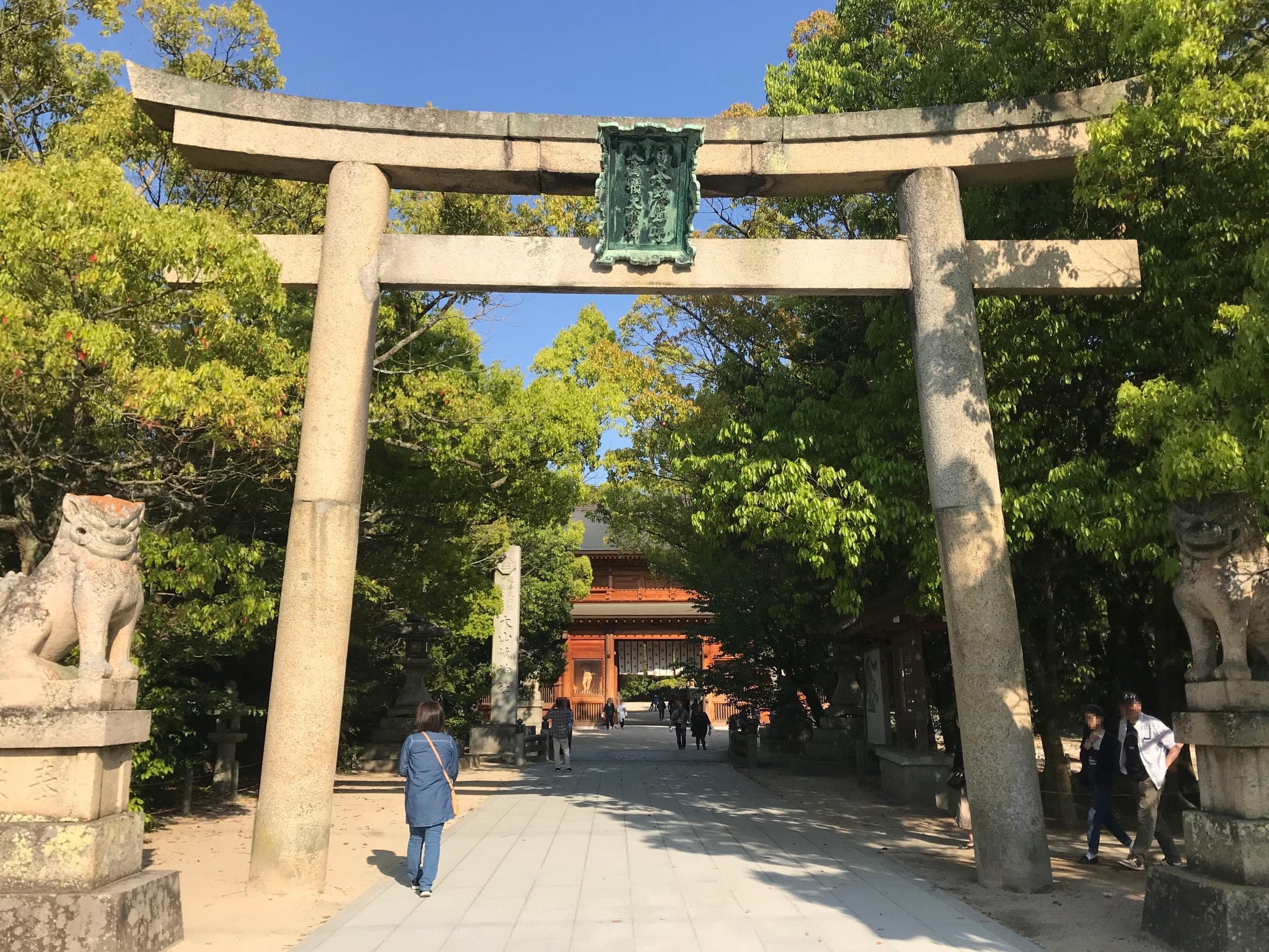 A stone torii opens the shaded approach to the gate of Oyamazumi Shrine on Omishima.