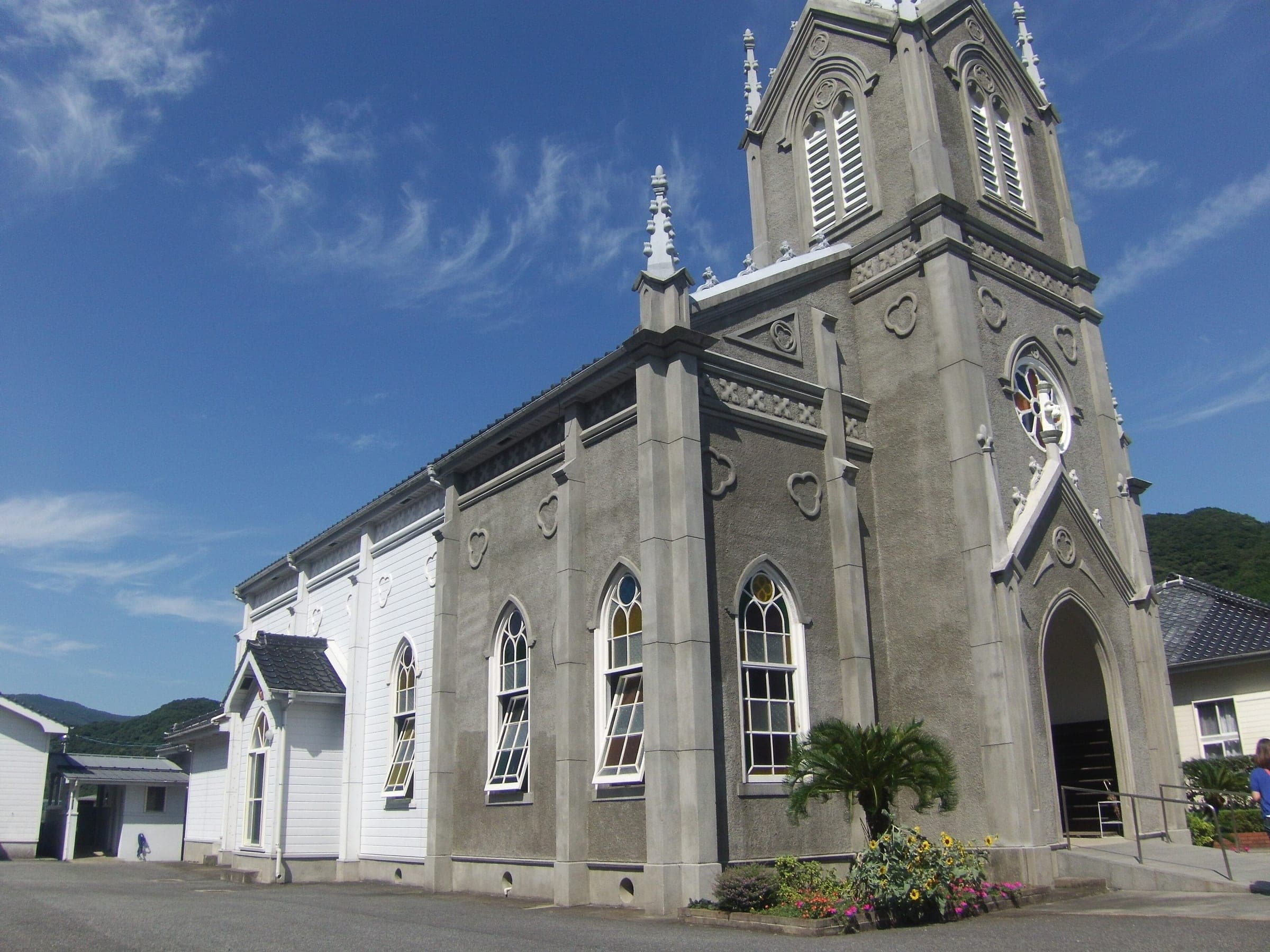 Sakitsu Church raises its grey Gothic spire above white walls under a blue sky in the Amakusa fishing village.