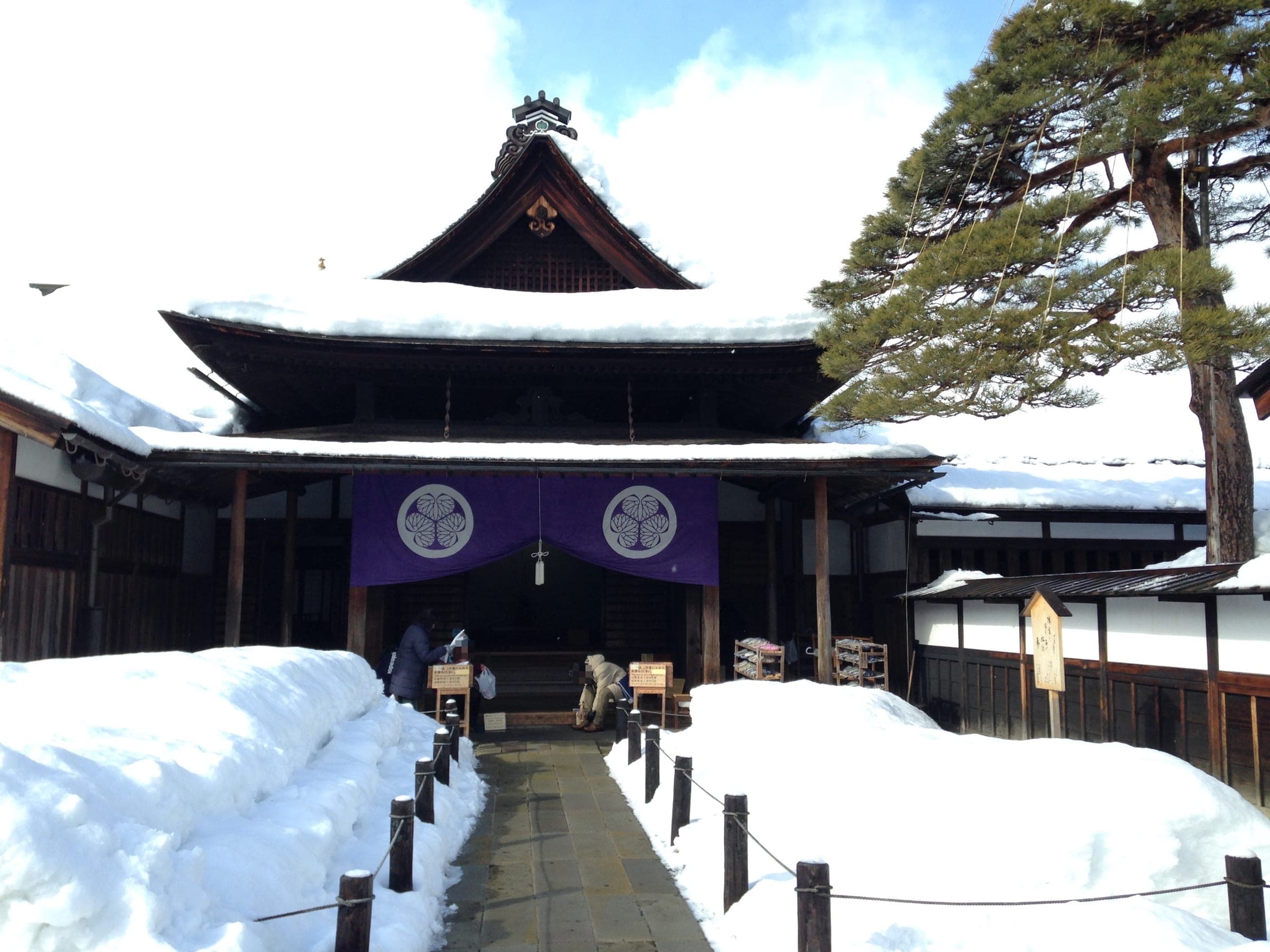 Snow lines the path to the main entrance of Takayama Jinya with its purple crested curtain