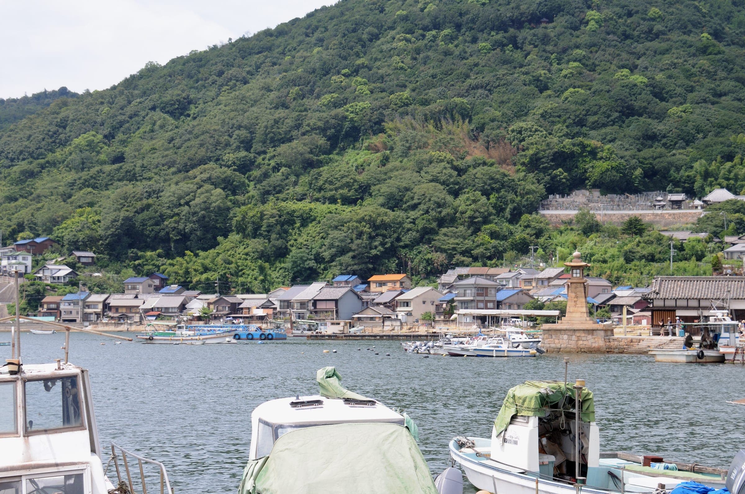 Fishing boats rest in Tomonoura harbour below the stone Joyato lantern and the wooded hill.