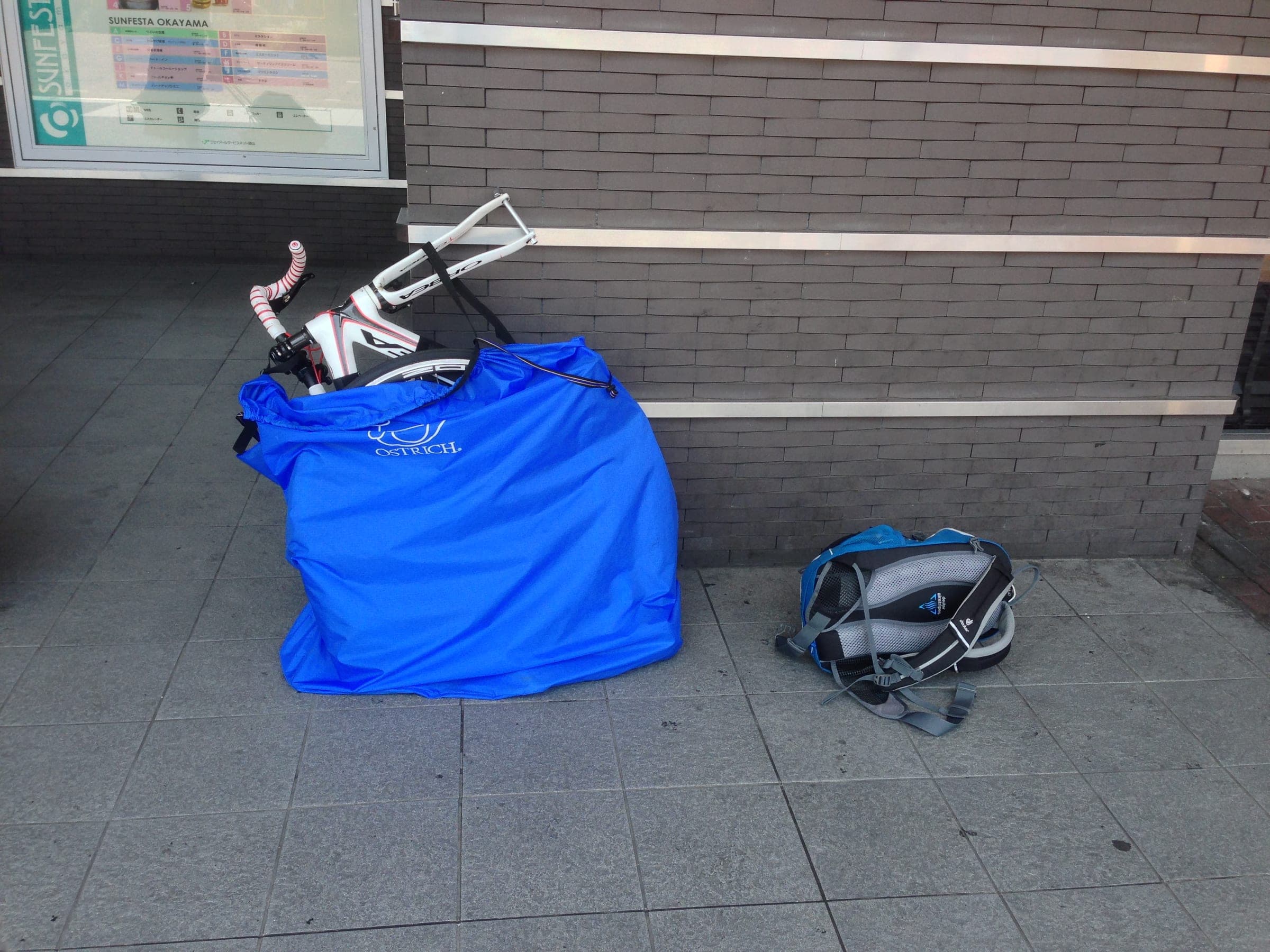 A road bike packed in a blue rinko bag waits beside a backpack at Okayama Station