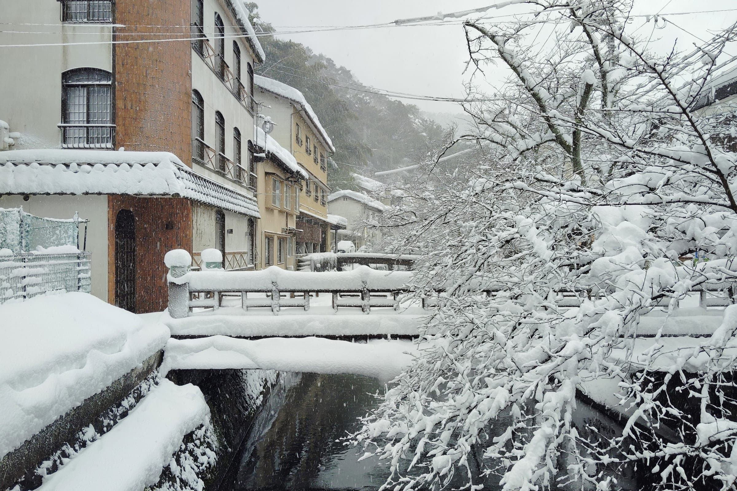 Snow piles on the stone banks and willows of the Otani River in Kinosaki Onsen in February