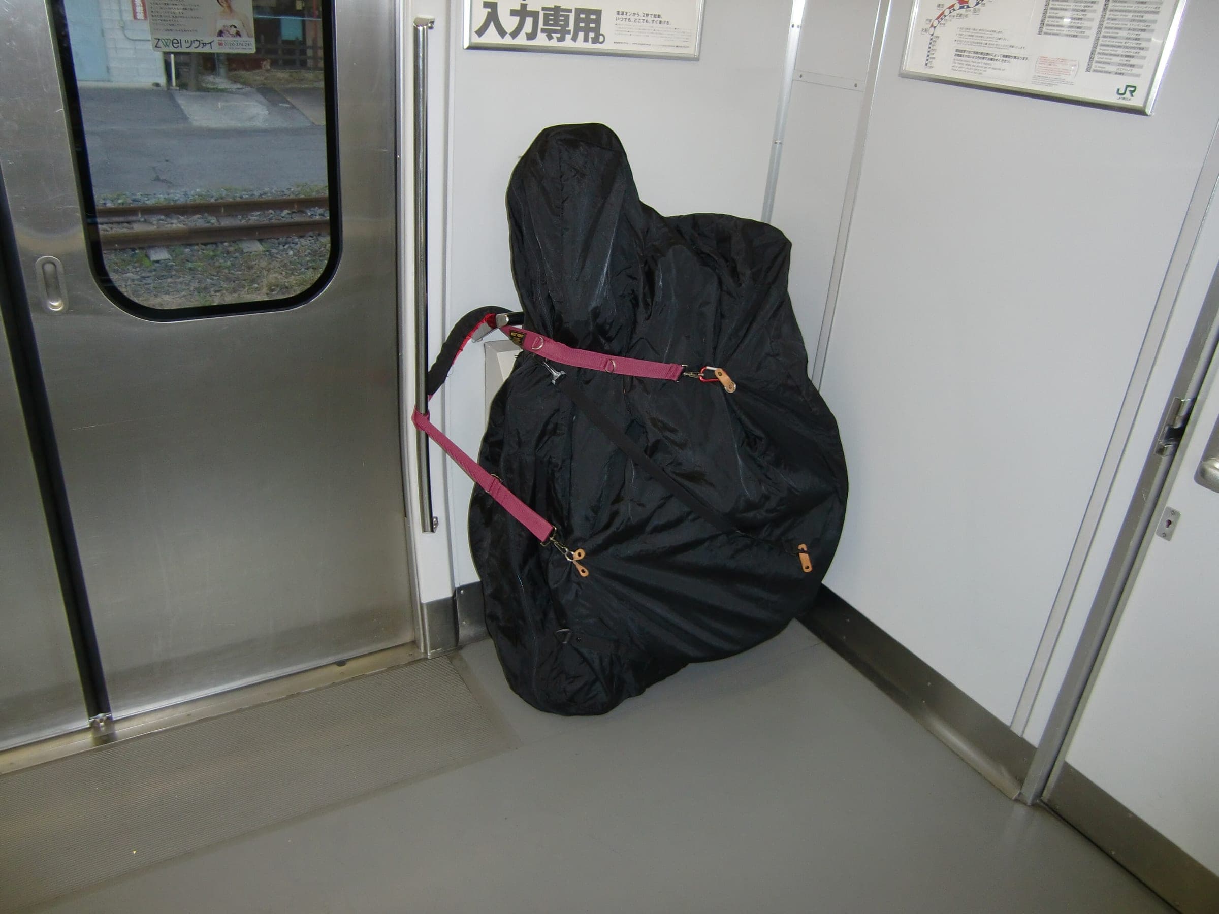 A bike in a black rinko bag stands strapped to a handrail by the doors of a JR commuter train