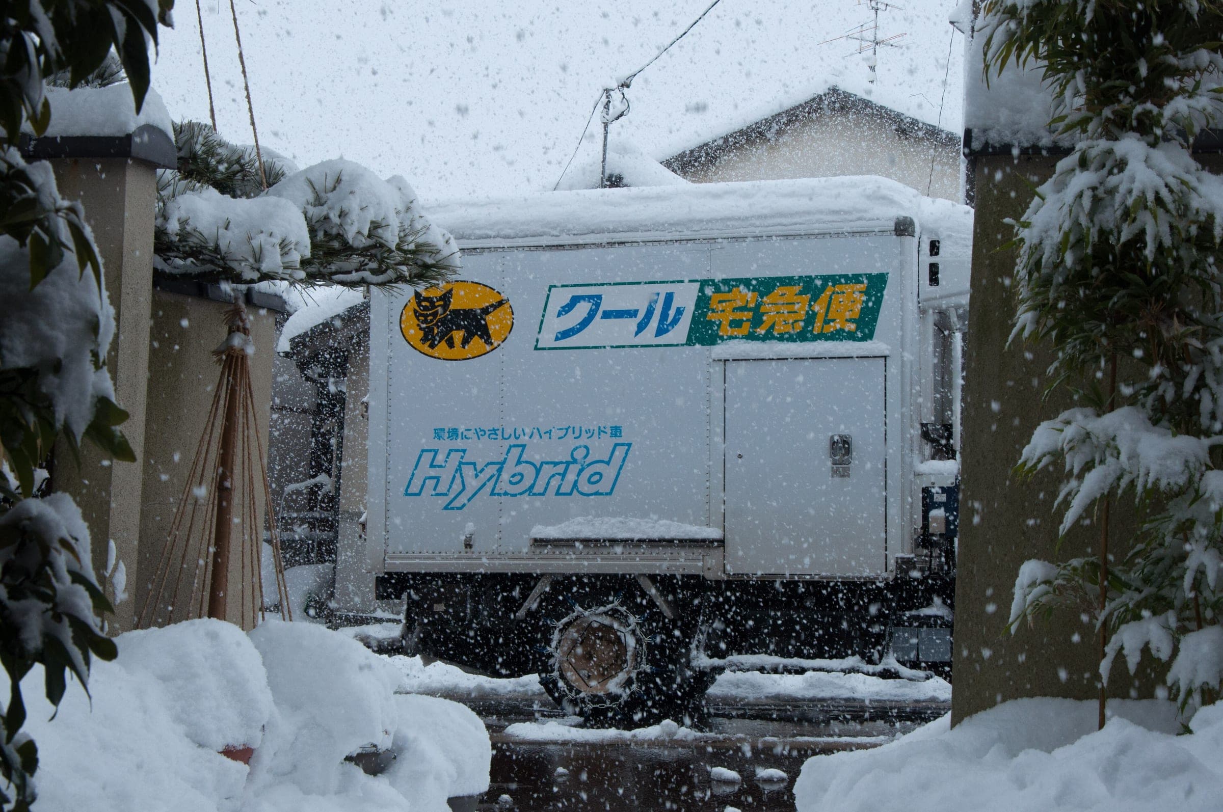 A Yamato Transport takkyubin truck waits in falling snow on a residential street in January