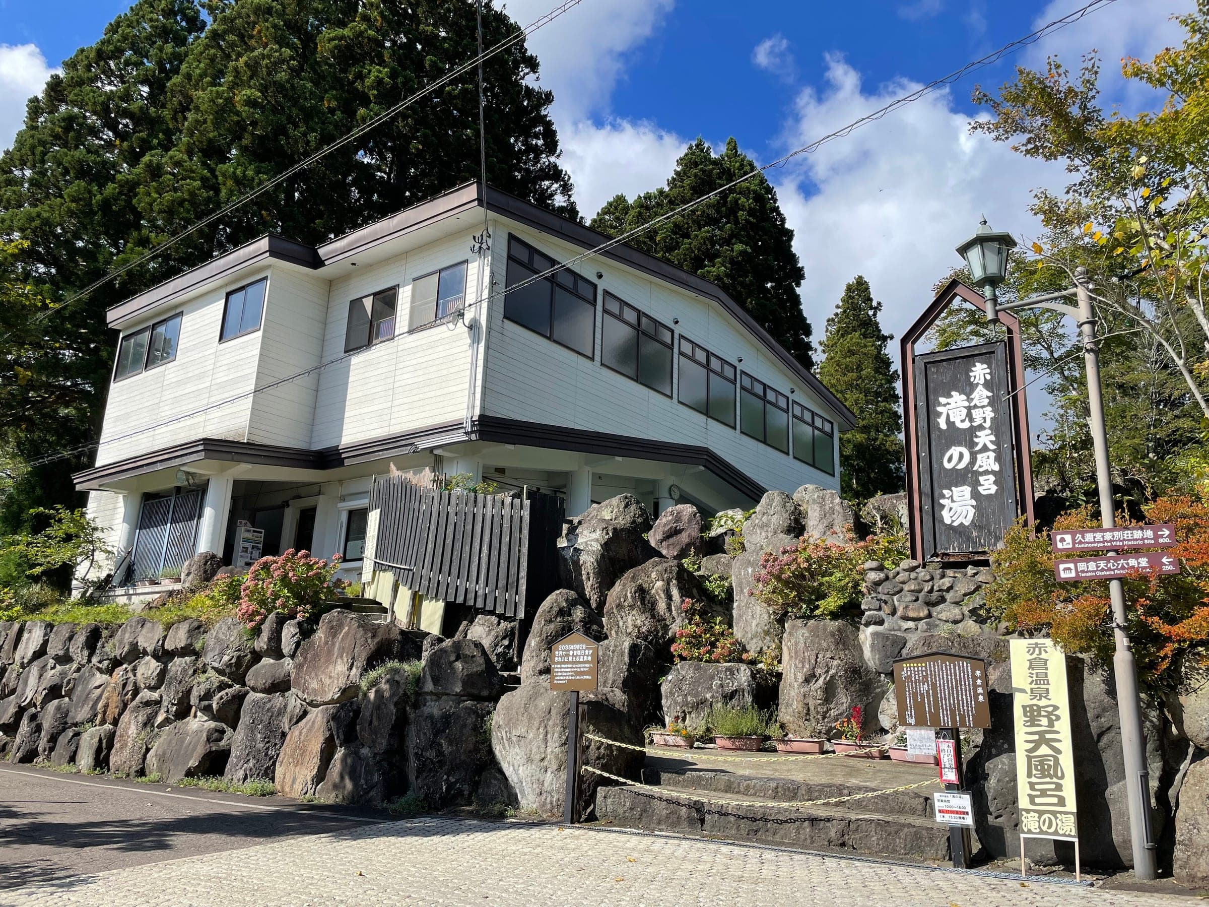 Taki no Yu's white bathhouse sits above a mossy stone wall at Akakura Onsen in October