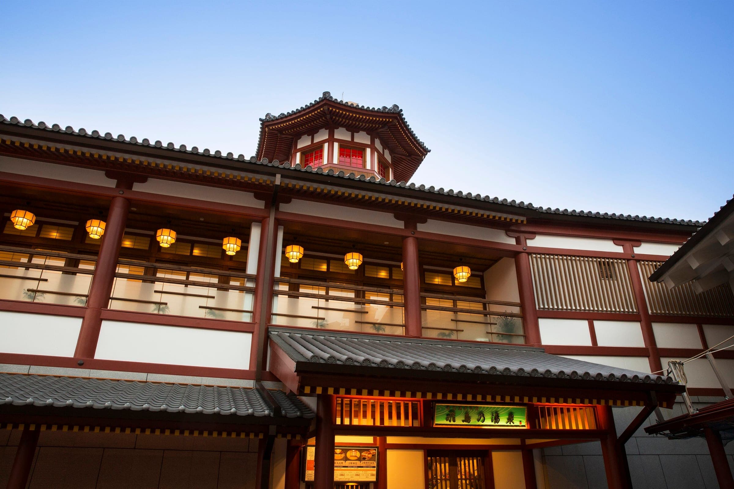 The front of Dogo Onsen Asuka-no-Yu glows under a clear evening sky in Matsuyama.