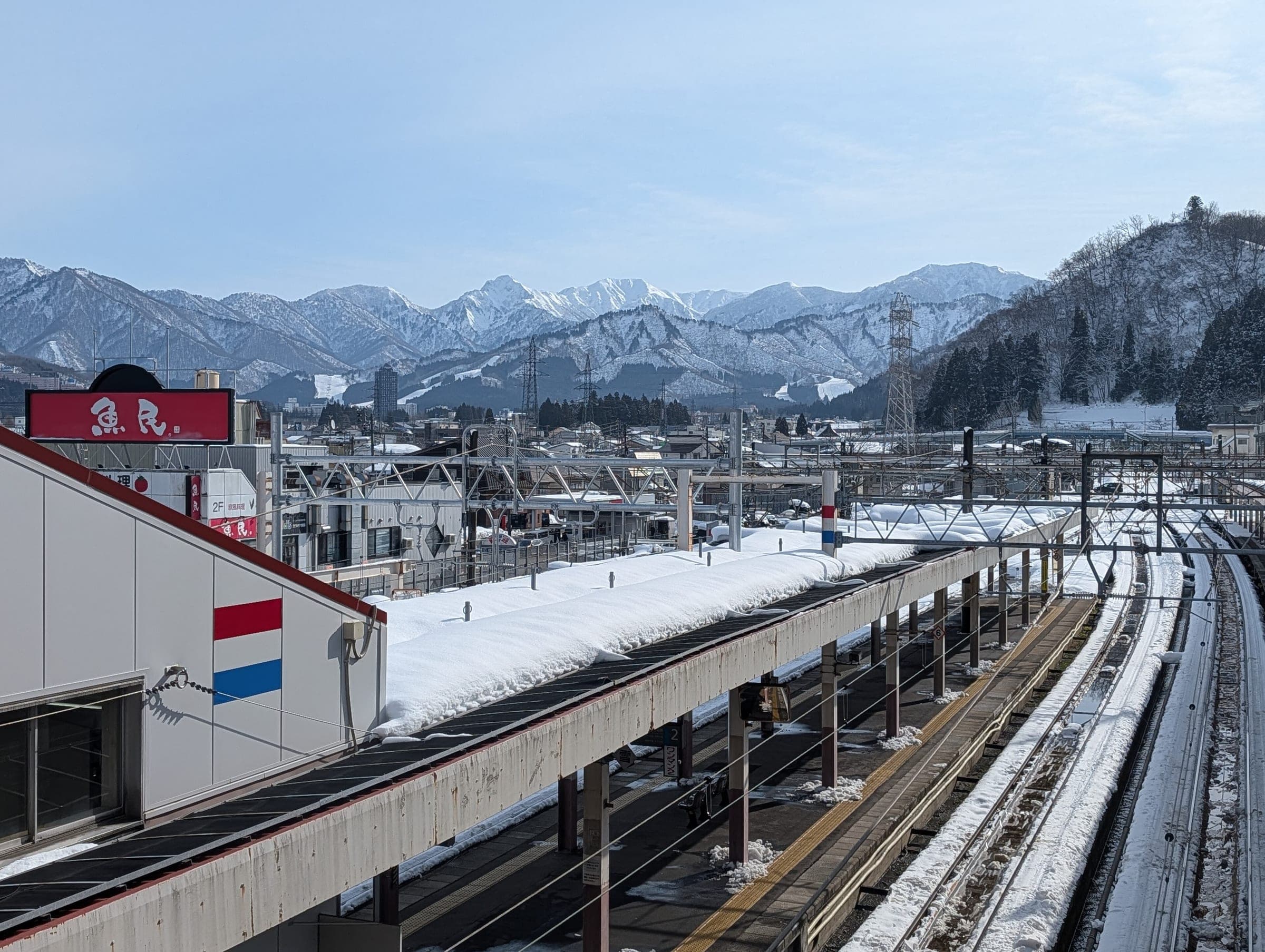 Snowy roofs of Echigo-Yuzawa spread below a white mountain range seen from the station