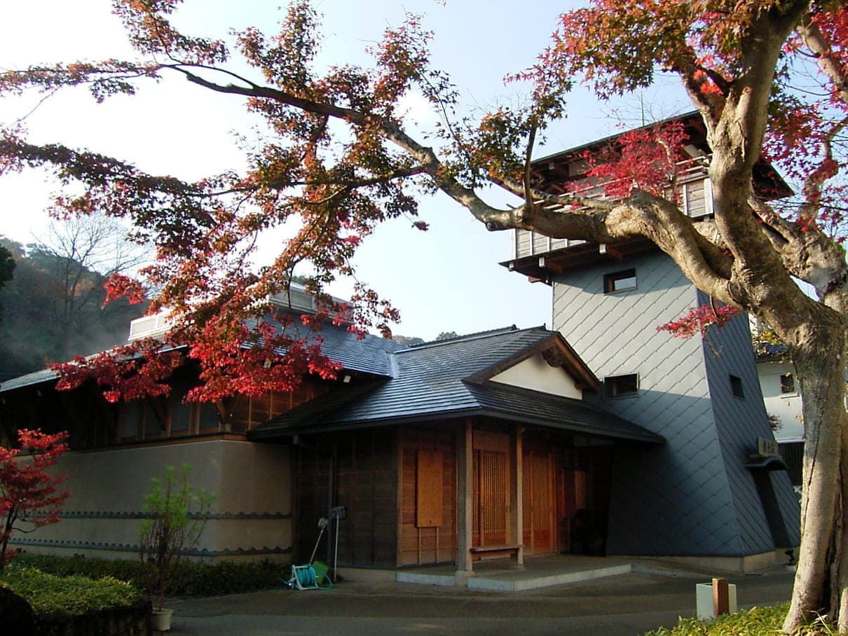 Red maple leaves frame the wooden bathhouse and lookout tower of Hako-yu in Shuzenji.