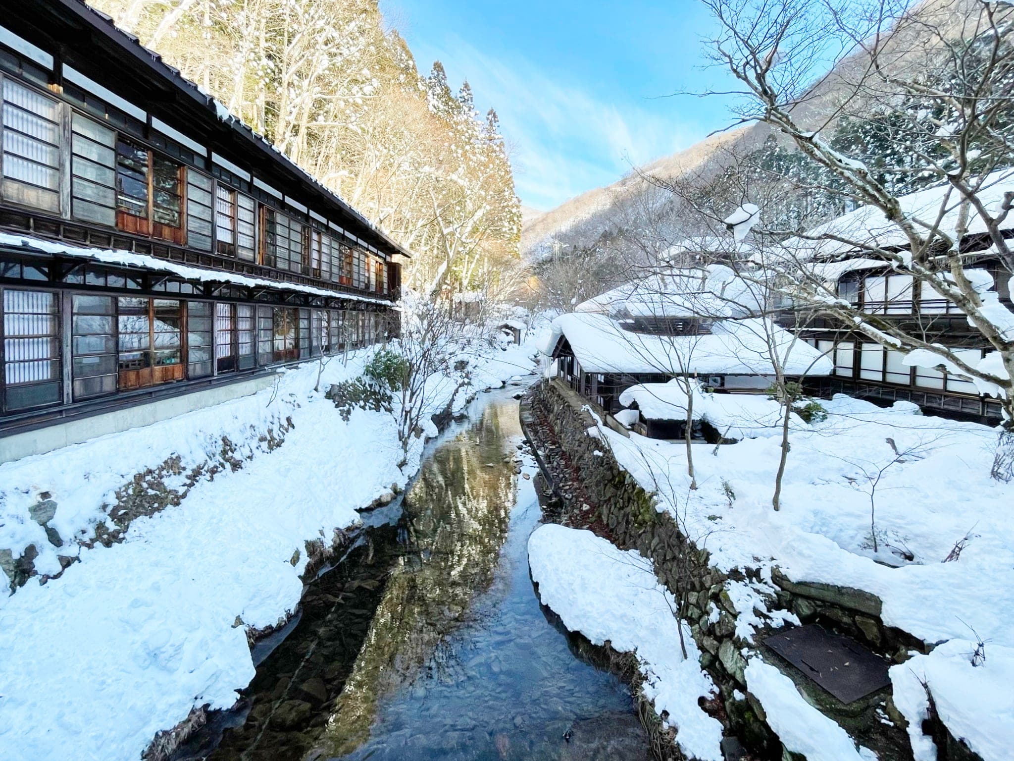 A clear stream runs between the snowy wooden wings of Chojukan at Hoshi Onsen