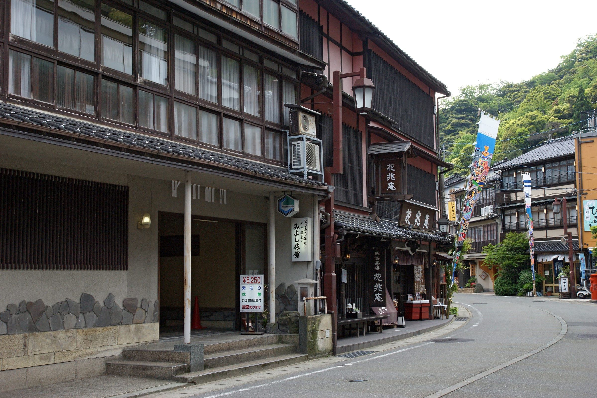 Three-storey timber ryokan line the main street of Kinosaki Onsen below the wooded hills
