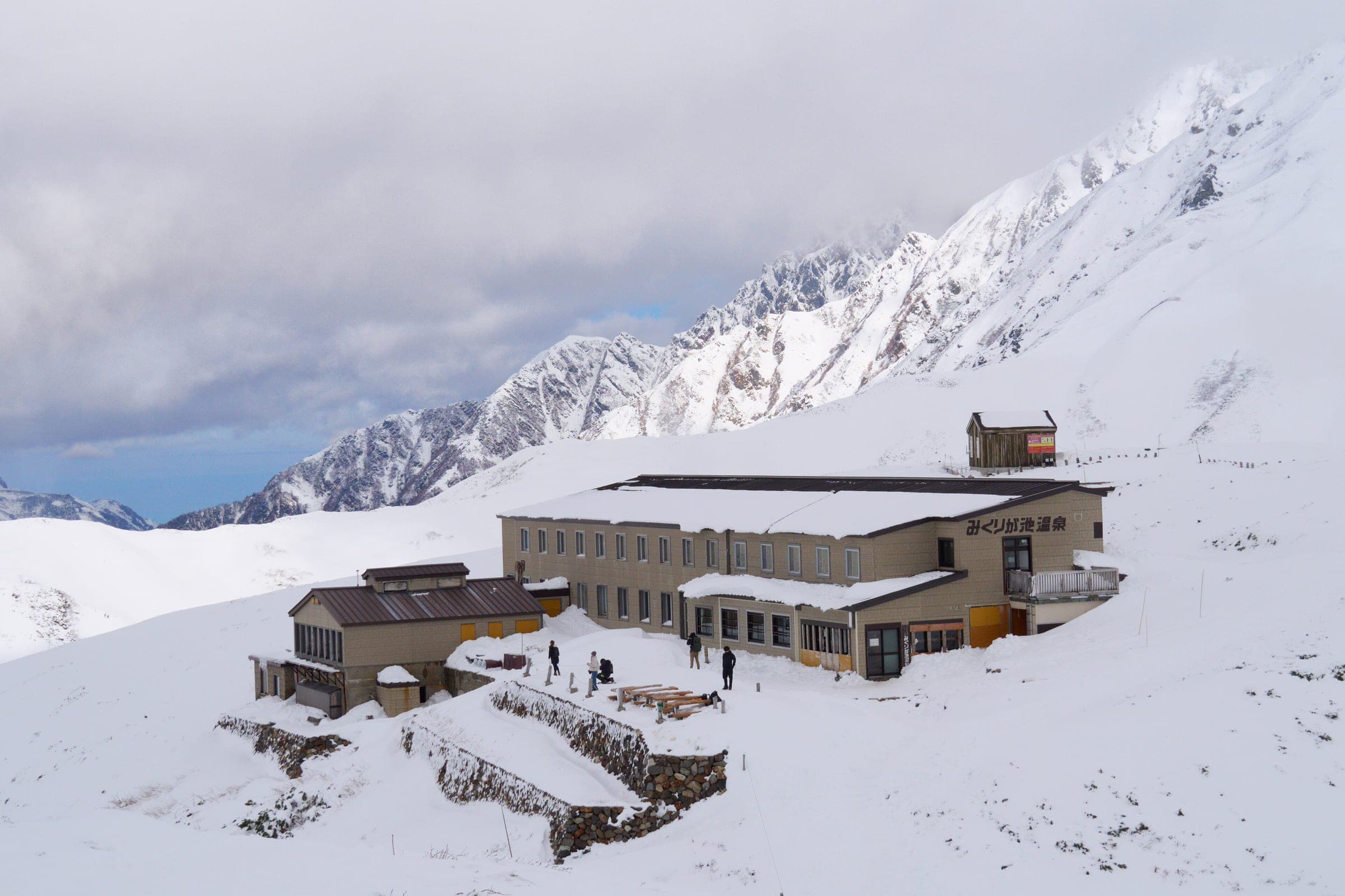 Mikurigaike Onsen's lodge stands in fresh snow below the jagged Tateyama ridge in November