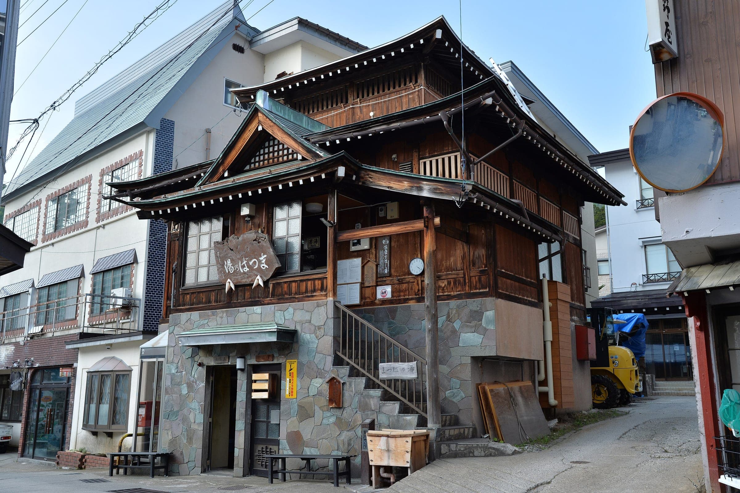 Matsuba-no-Yu stands on a stone base at a lane corner in Nozawa Onsen, with stairs up to its door.