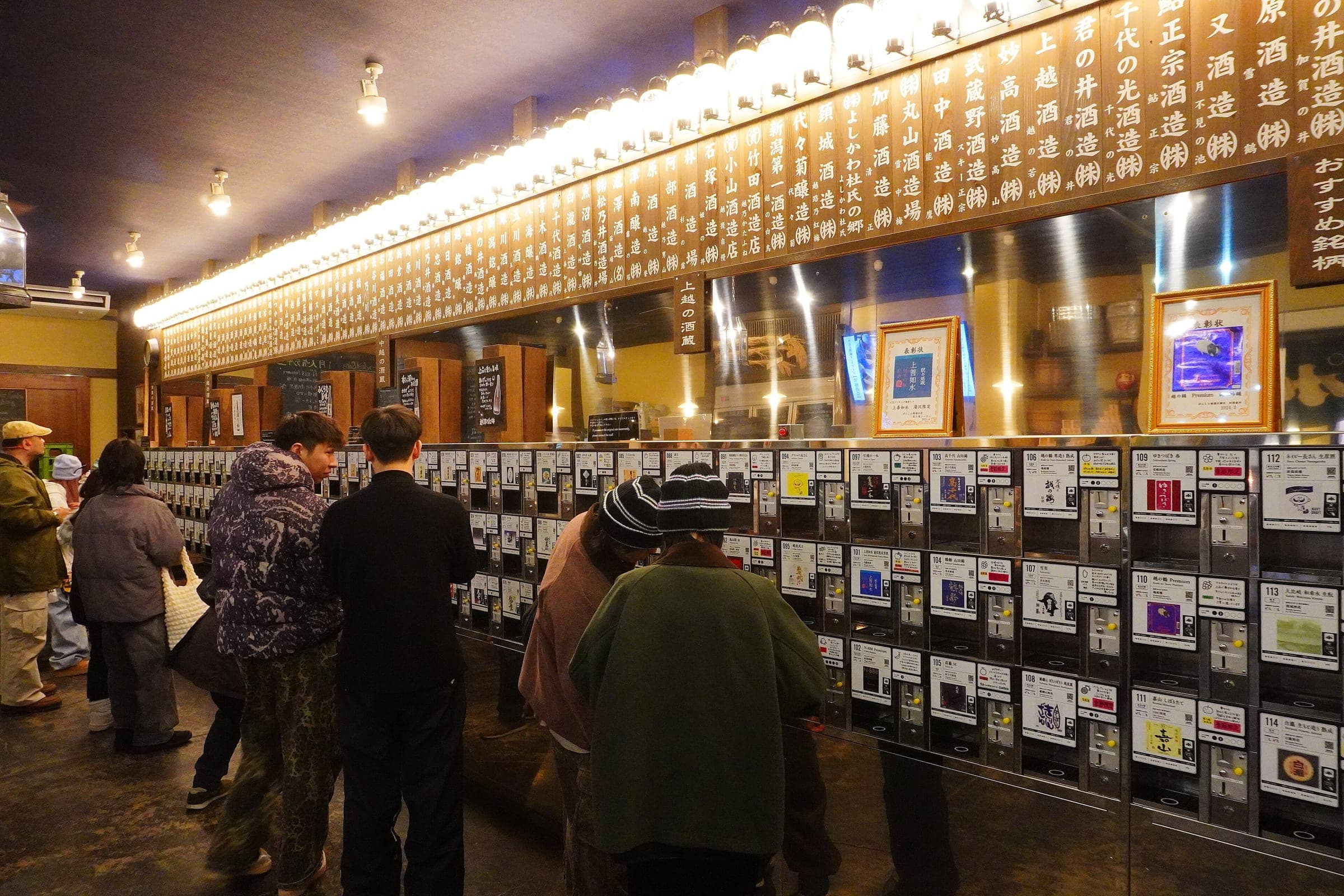 Visitors browse the long wall of sake tasting machines at Ponshukan in Echigo-Yuzawa Station