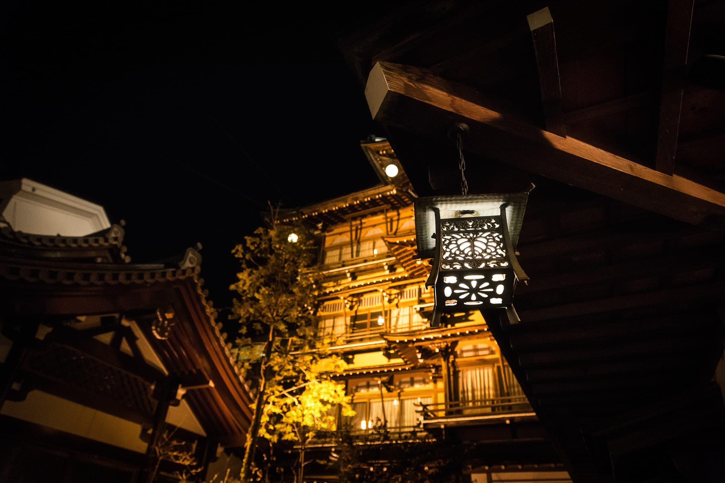 An iron lantern hangs in front of the lit wooden storeys of the Kanaguya inn at Shibu Onsen.