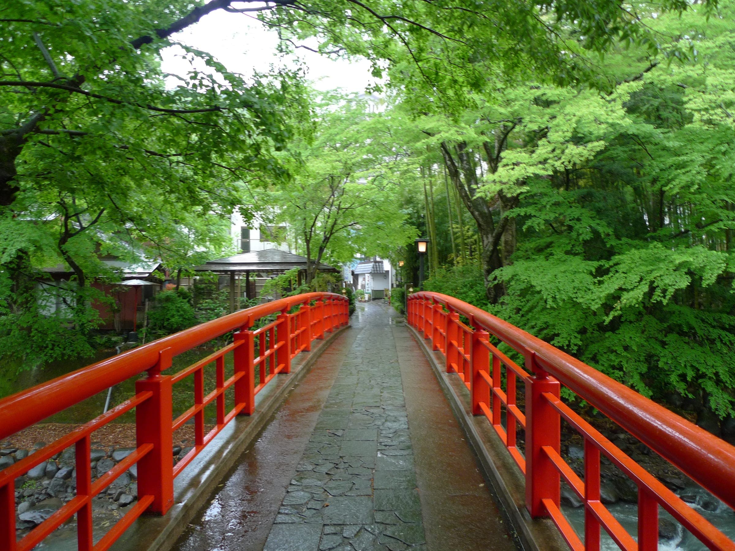 A red footbridge crosses the river into fresh spring maples at Shuzenji Onsen.