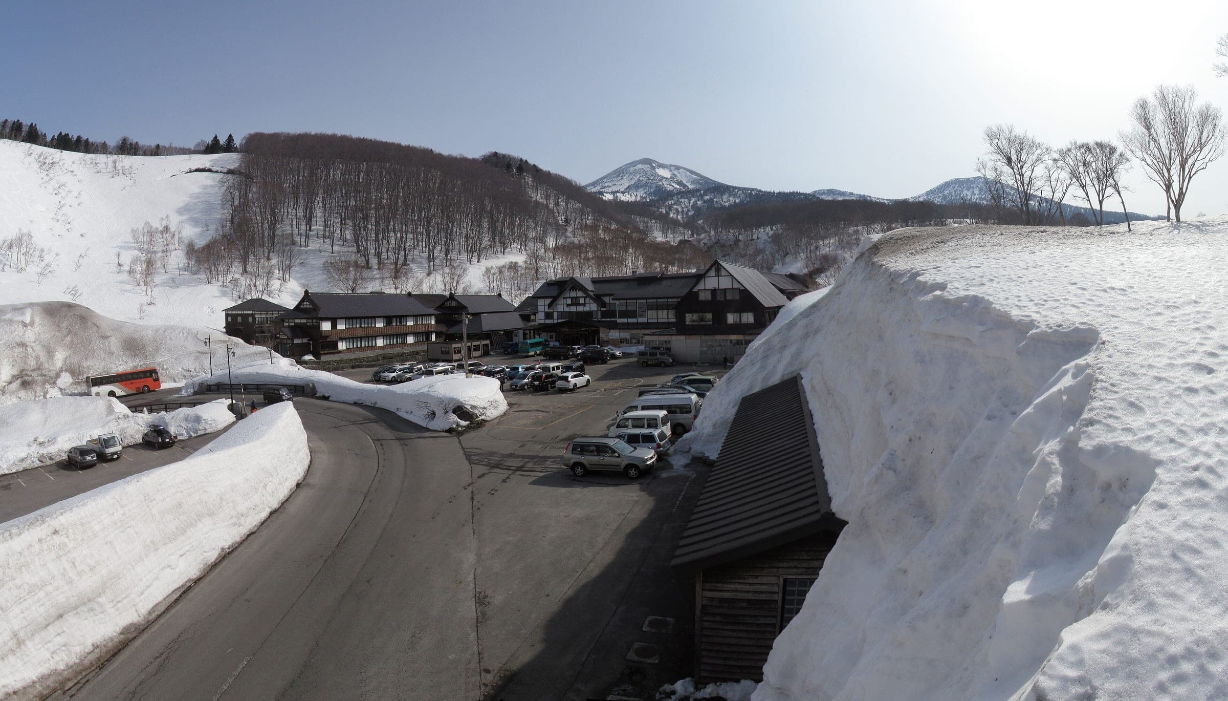 Snow walls taller than the eaves surround the Sukayu Onsen buildings below the Hakkoda peaks in March.