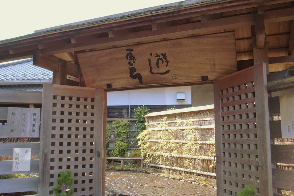 A wooden gate with a lattice screen marks the entrance to Tenzan Tohji-kyo in Hakone Yumoto.