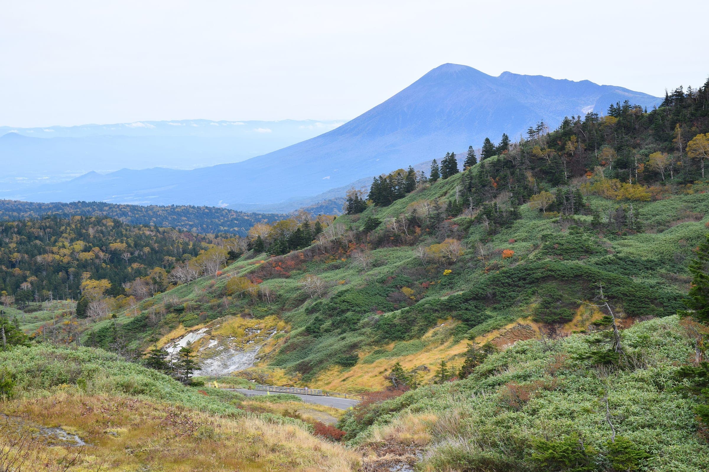 Autumn scrub covers the Hachimantai plateau near Toshichi Onsen as Mount Iwate rises in the haze.