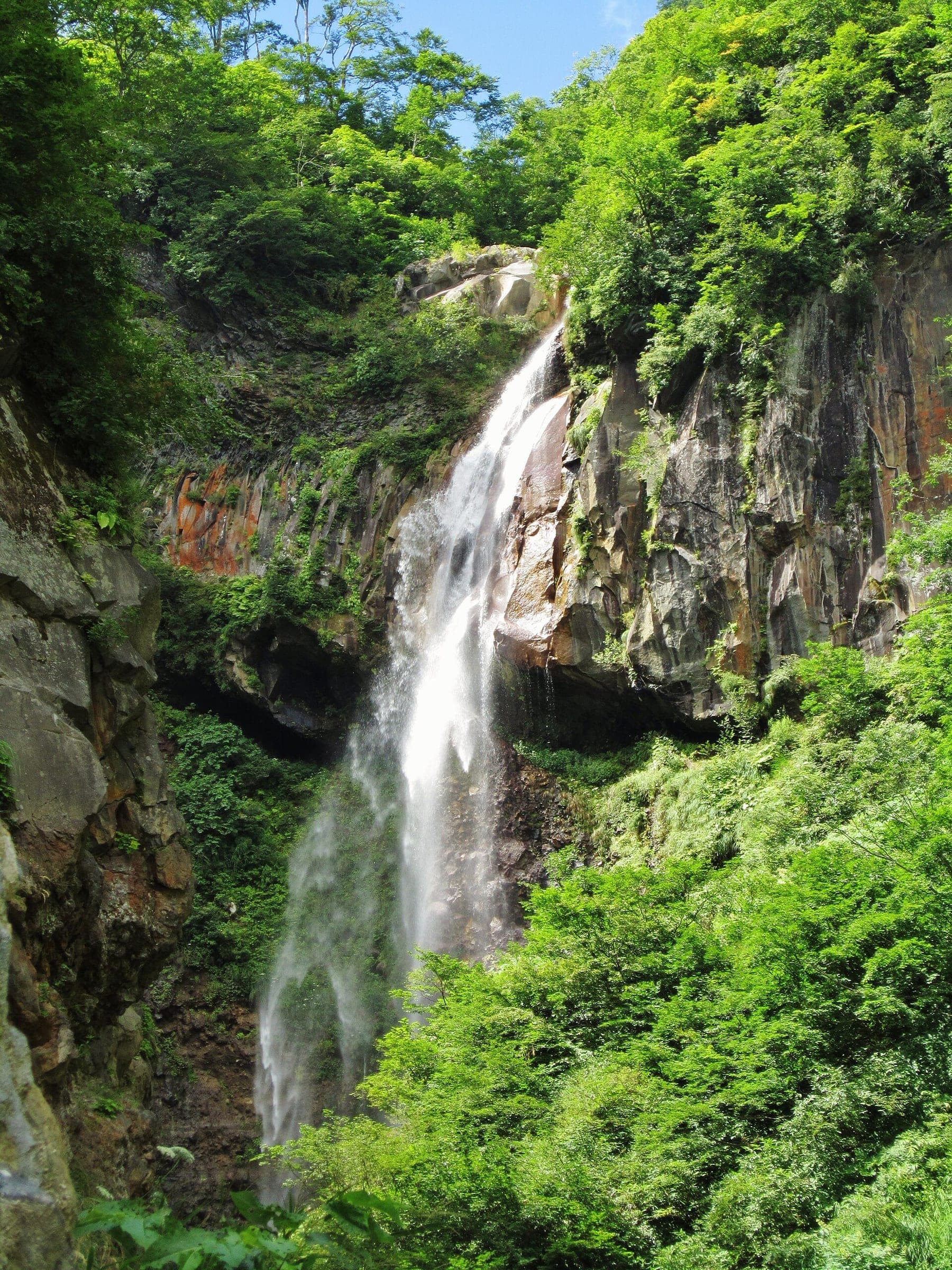 So Falls drops down a dark cliff in thick summer forest on the trail above Tsubame Onsen