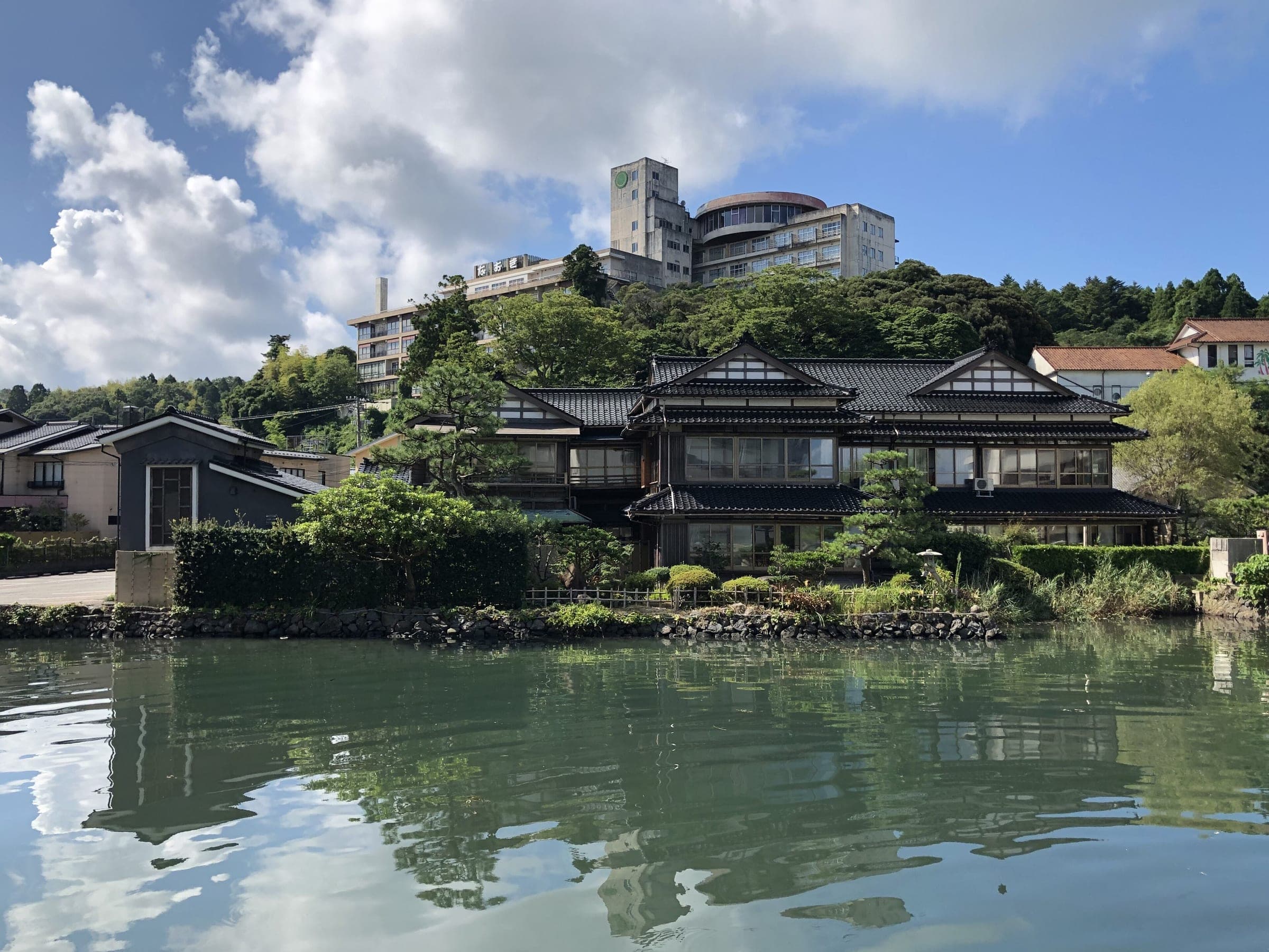 A tiled-roof ryokan sits on the waterfront at Wakura Onsen with hotels on the hill behind