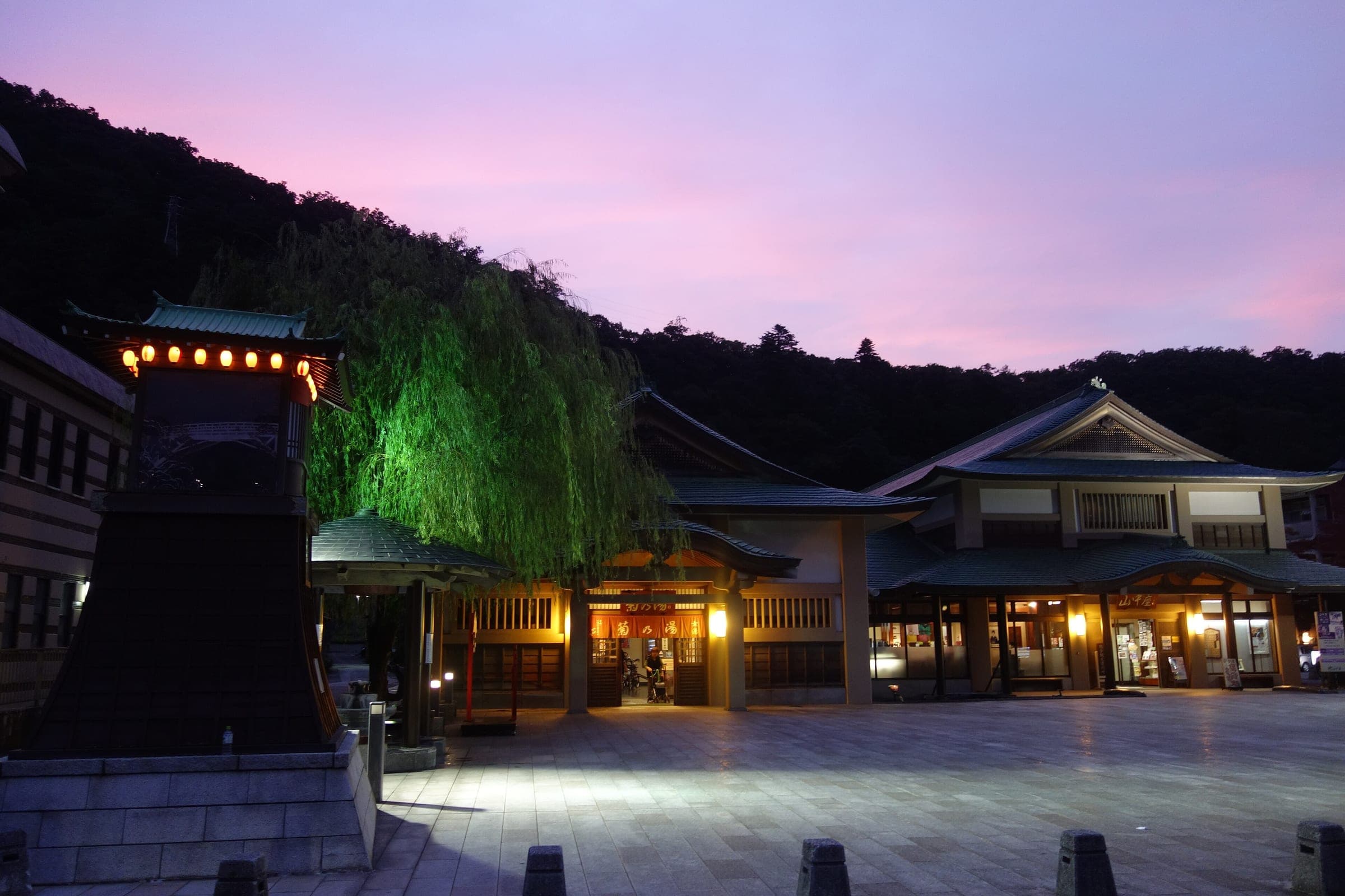 Lanterns glow outside the Kikunoyu public bathhouse in Yamanaka Onsen under a pink dusk sky