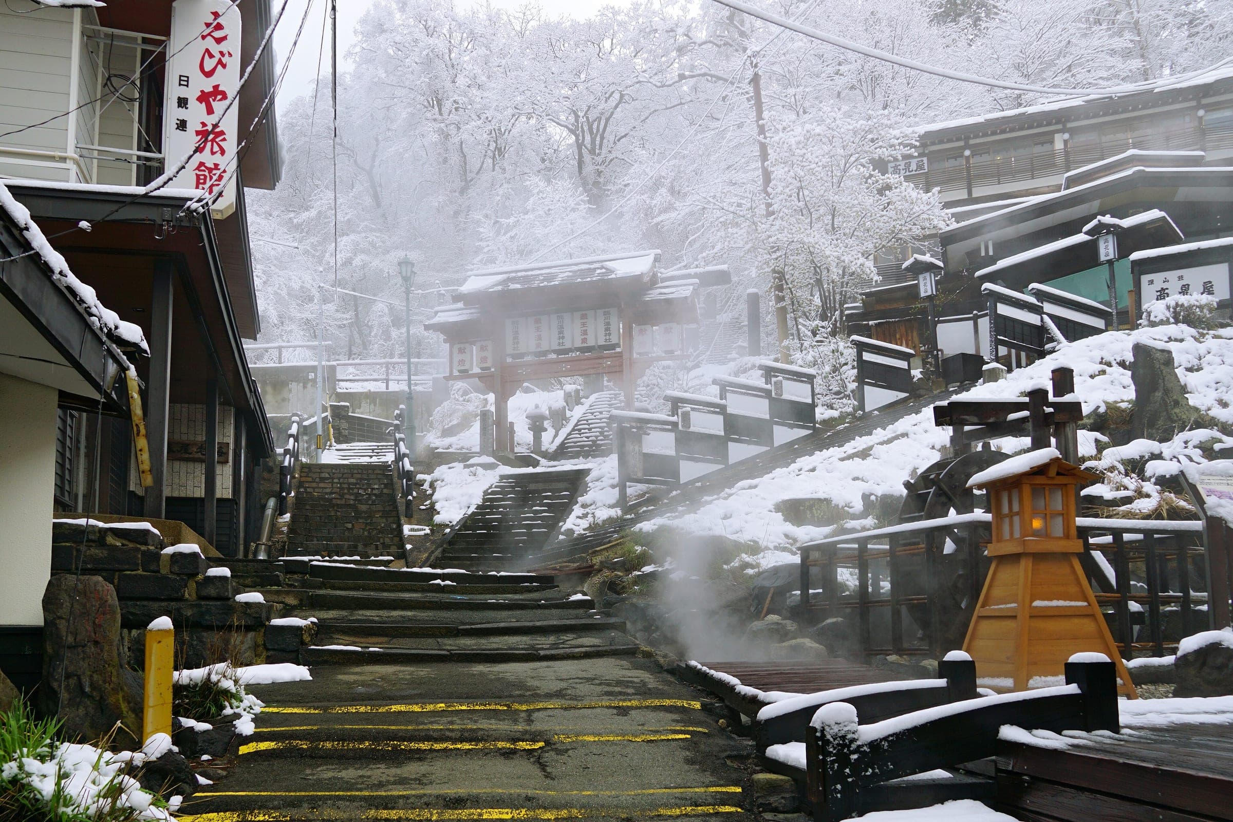 Hot spring water steams beside stone steps in Zao Onsen as fresh snow coats the trees.