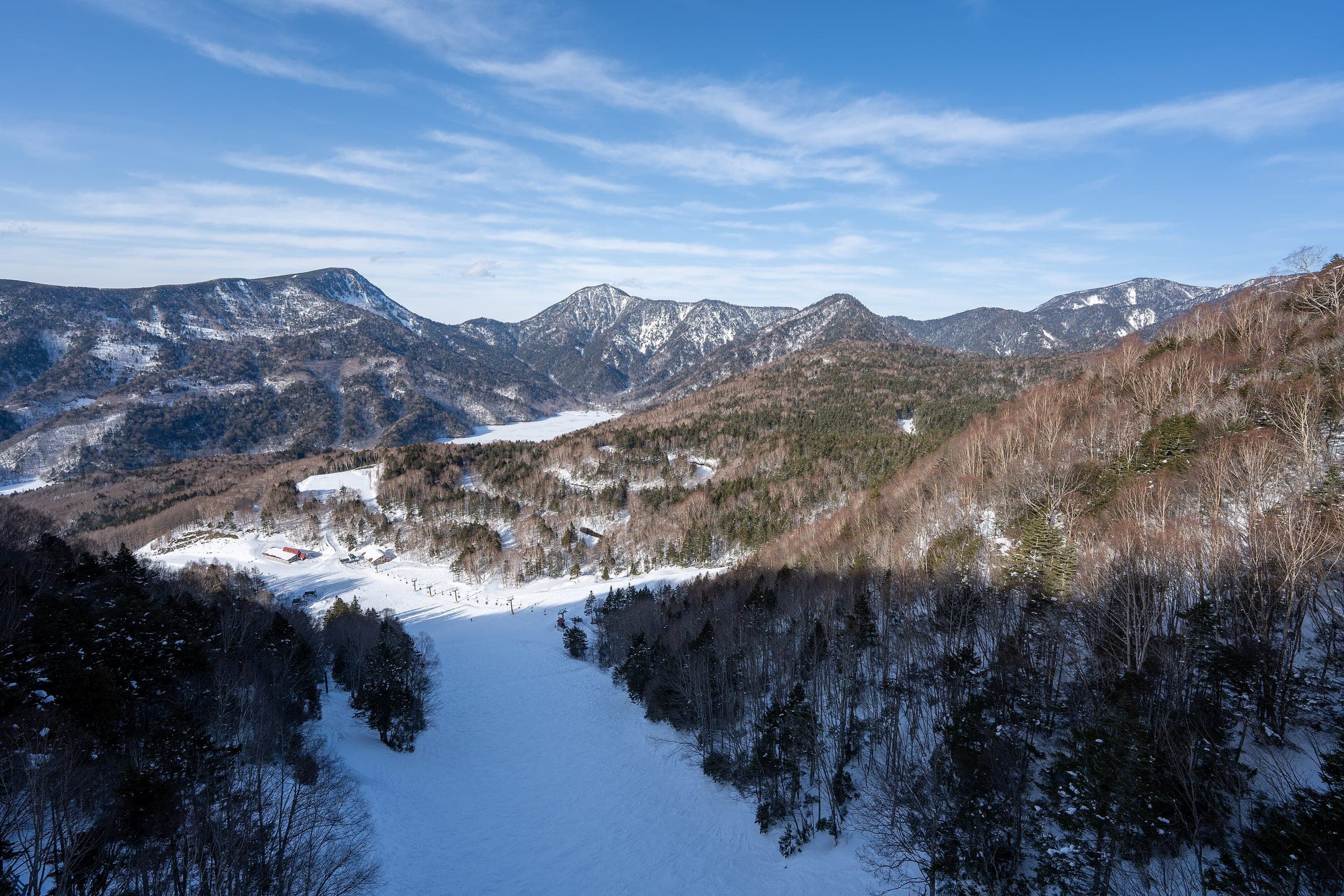 Groomed runs at Marunuma Kogen drop through forest below snowy peaks in Gunma's Katashina area
