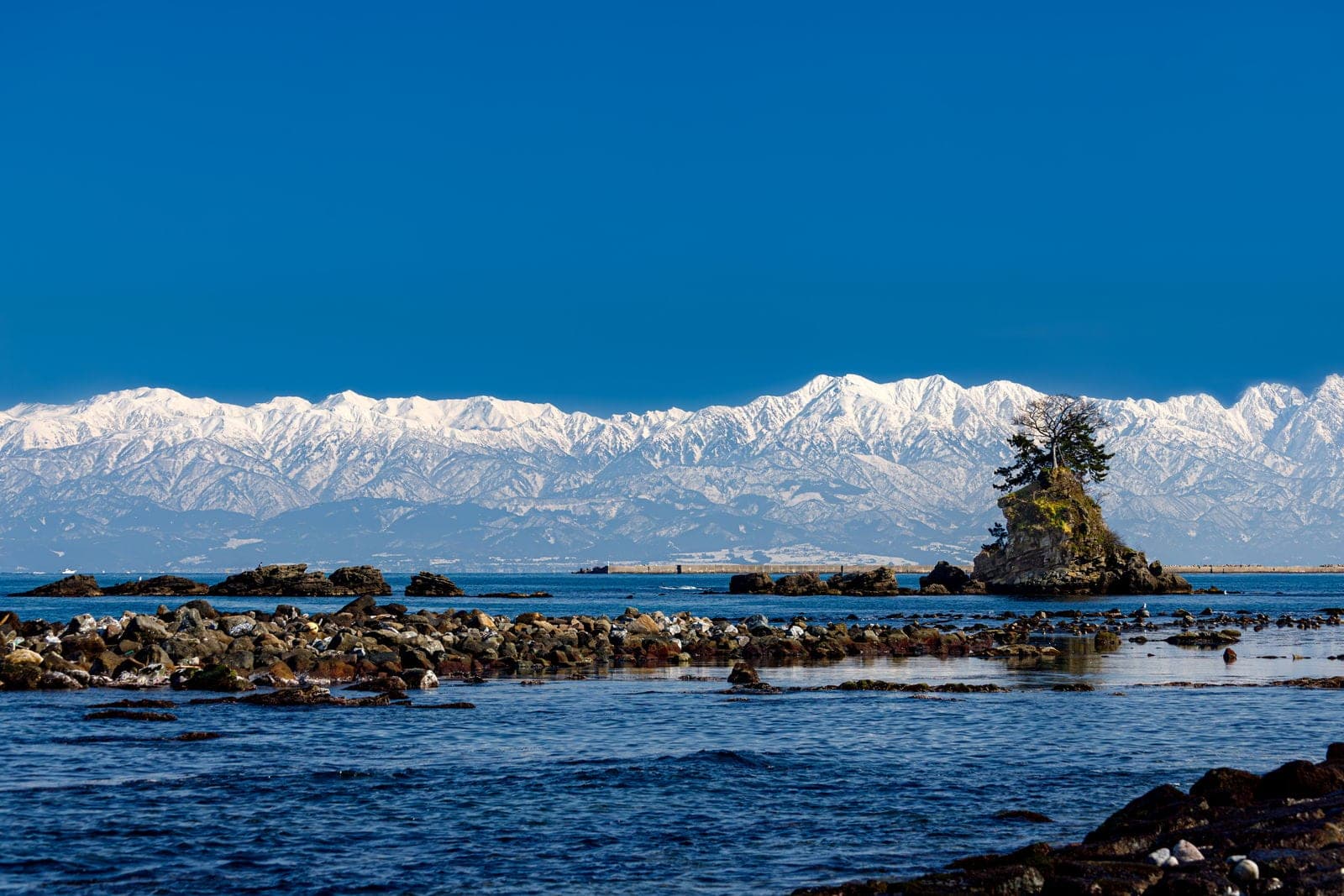 The snowy Tateyama range stands across Toyama Bay behind the pine-topped Onna-iwa rock at Amaharashi