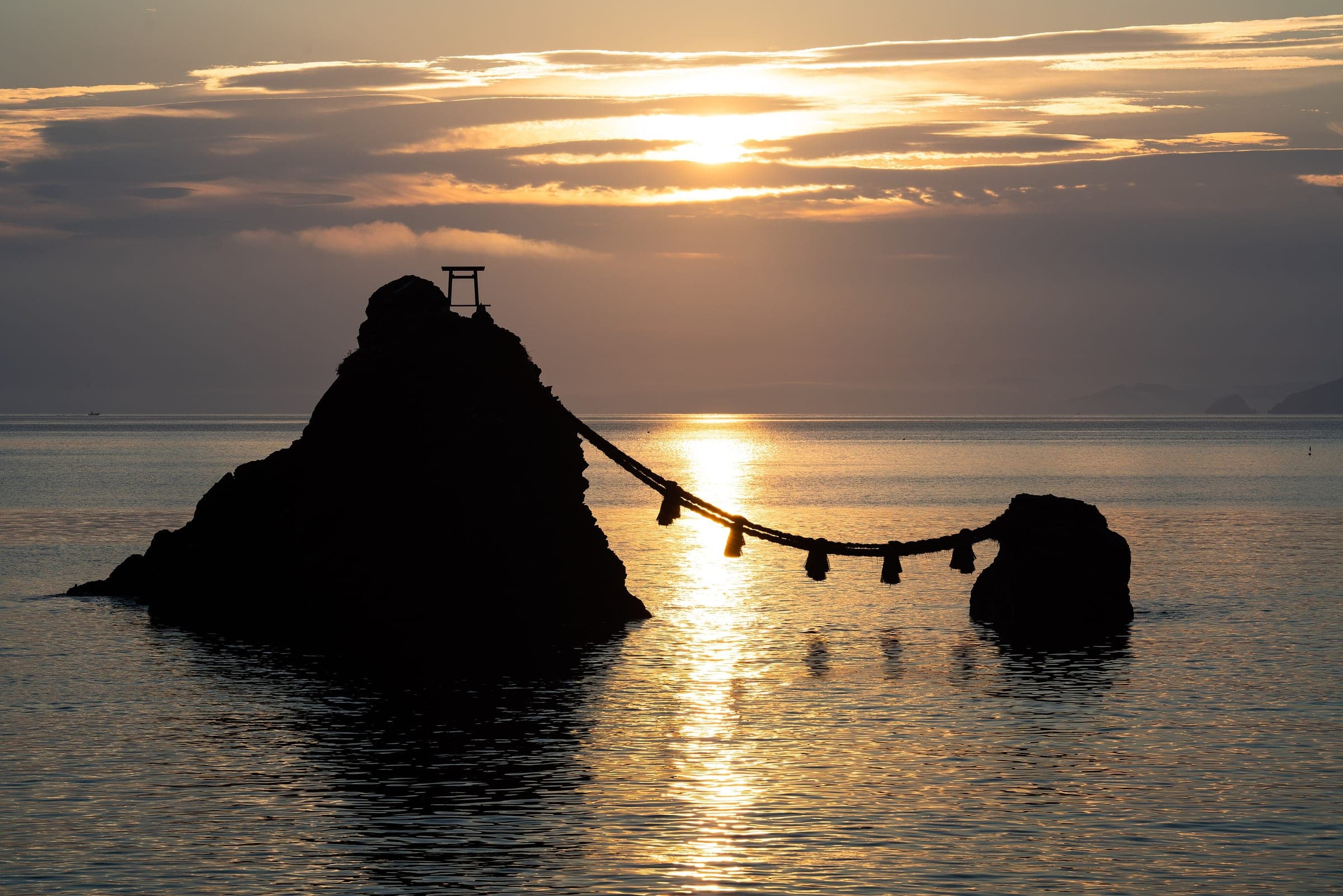 The sun rises behind the rope-linked Meoto Iwa rocks off Futami on Ise Bay in July