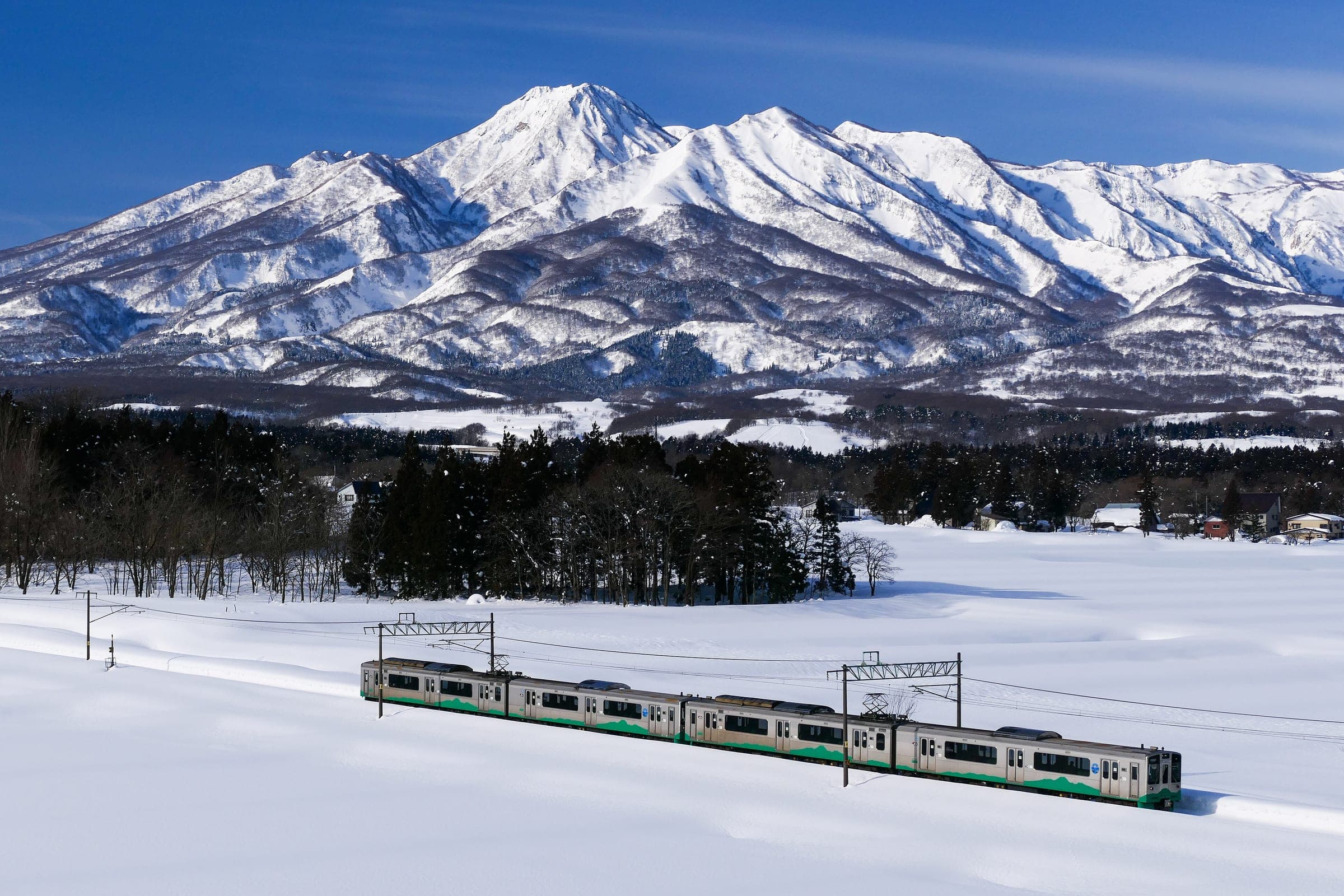 A Myoko Haneuma Line train crosses snowfields below the white bulk of Mount Myoko in Niigata