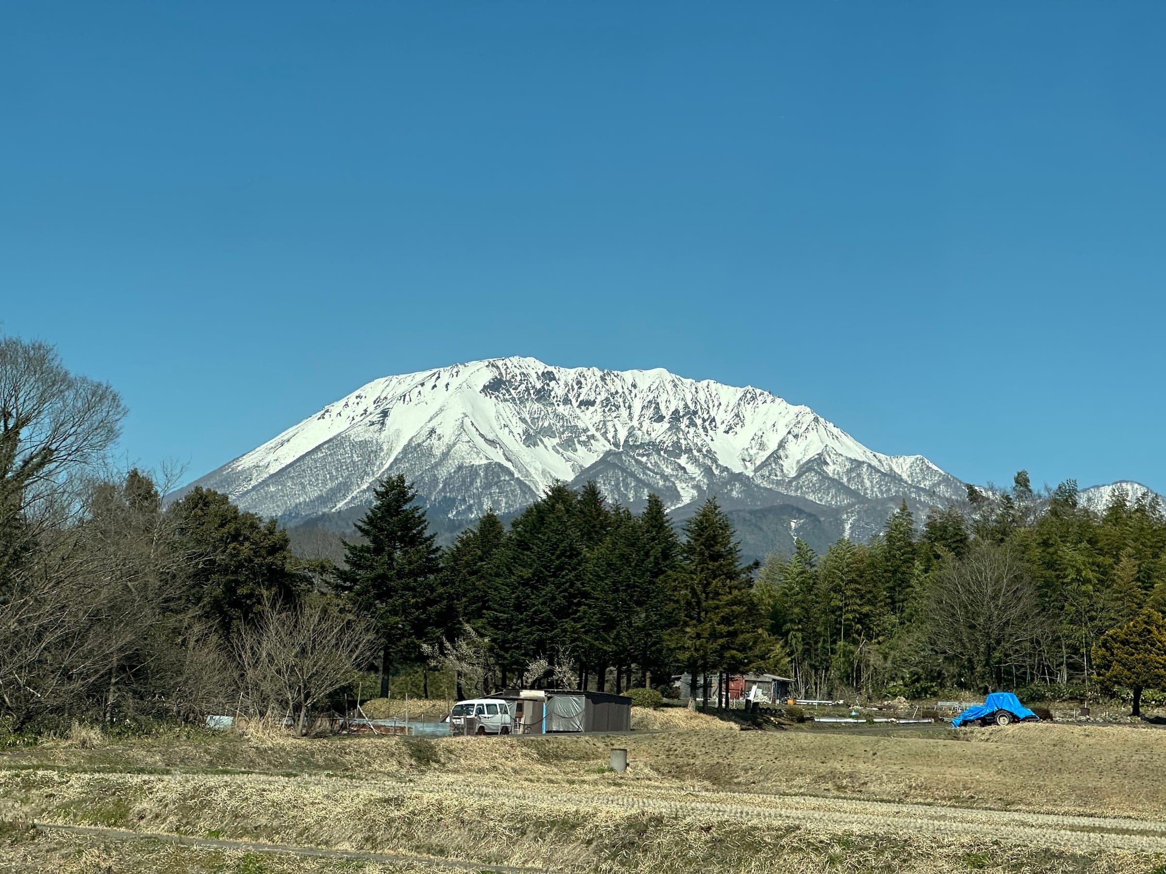 Snow still covers the north face of Daisen above cedar woods and fields near Yonago in March