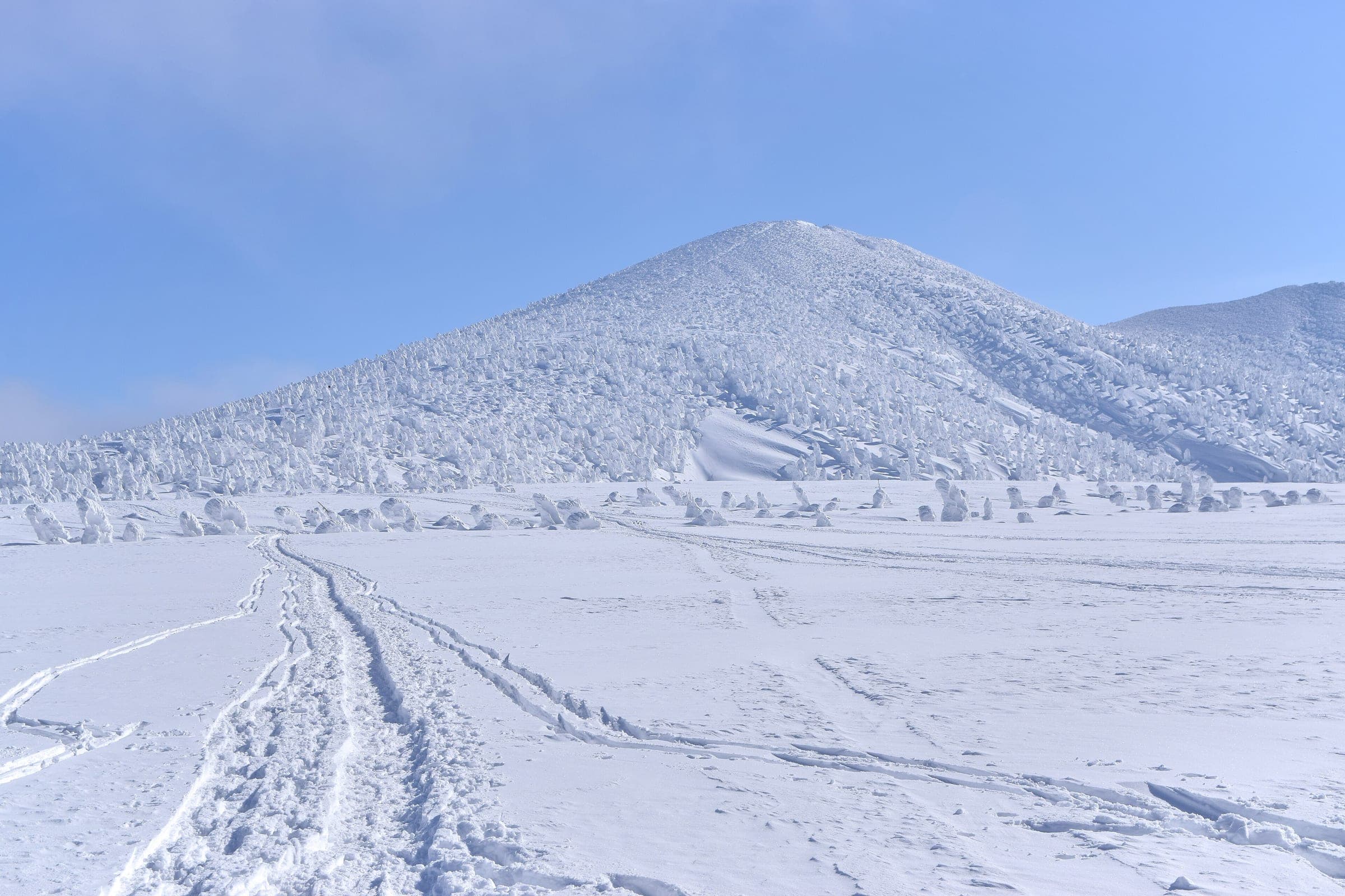 Ski touring tracks cross the snowfield below a rime-covered peak of the Hakkoda range in Aomori
