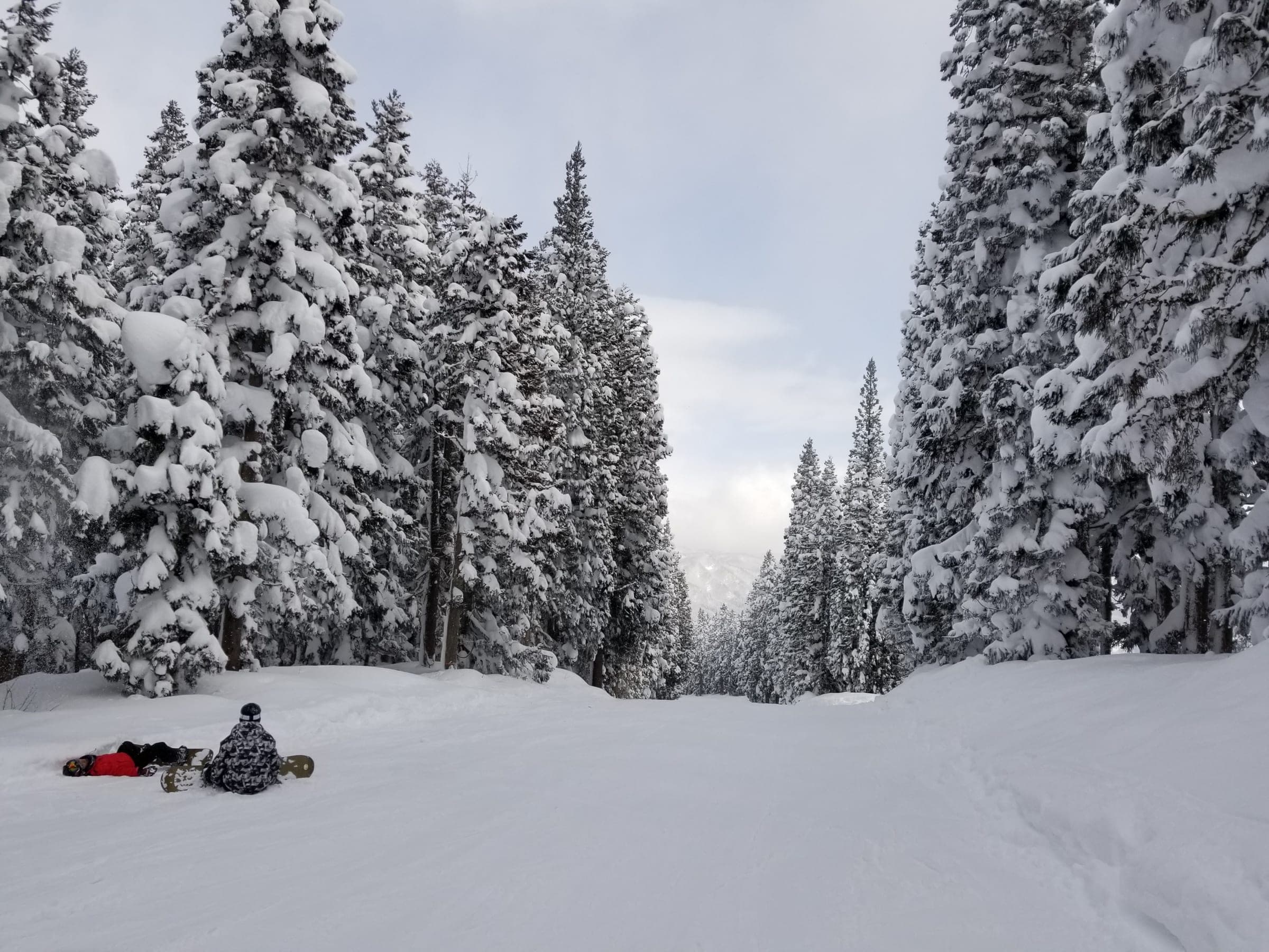 Snowboarders rest on a run lined with heavy snow-covered conifers at Akakura Onsen Ski Area