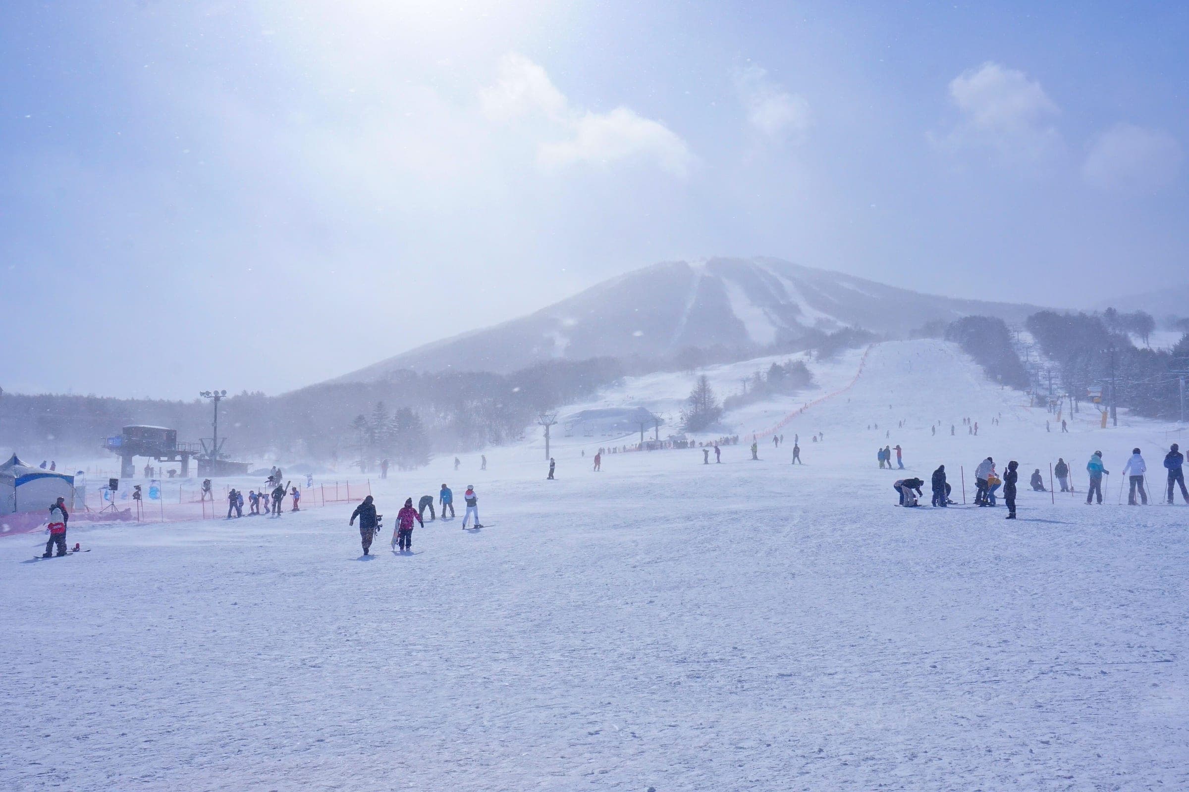 Skiers and snowboarders spread across the APPI base slopes as snow blows in under Mount Maemori.