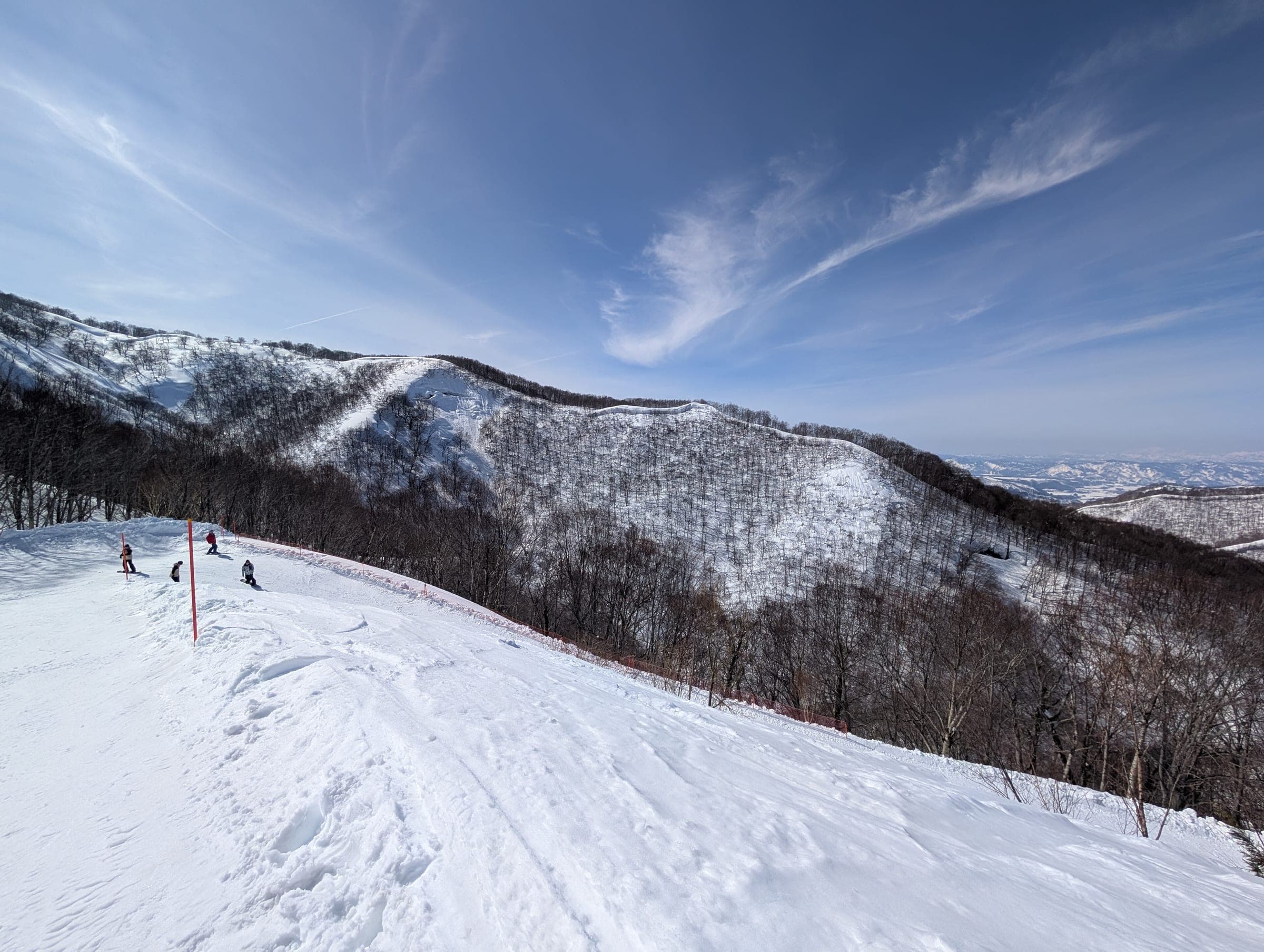 Skiers pause on a ridge run at GALA Yuzawa with snowy forested hills beyond